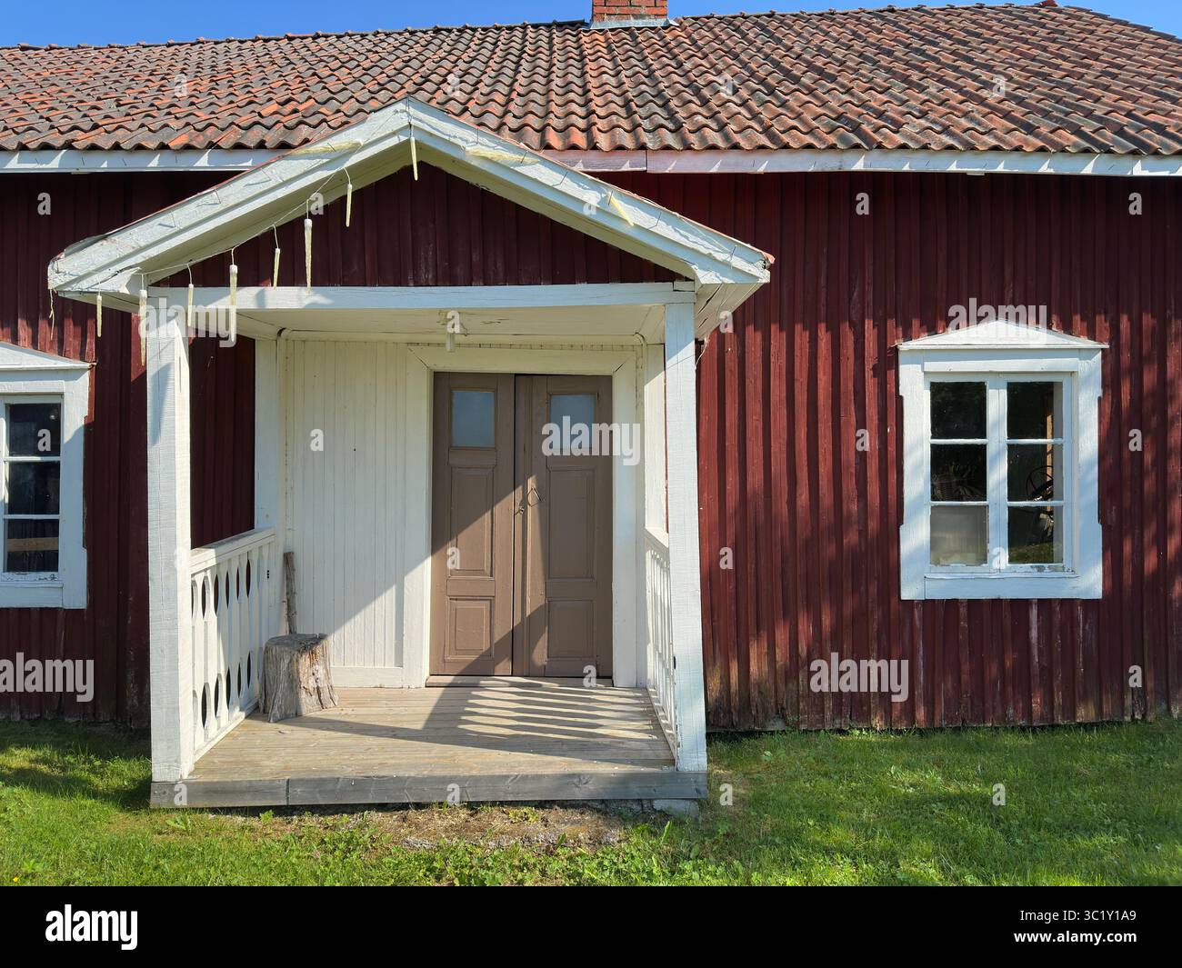 Bezauberndes rotes Haus mit einer weißen Veranda und einer rustikalen Atmosphäre an einem sonnigen Tag. Stockfoto