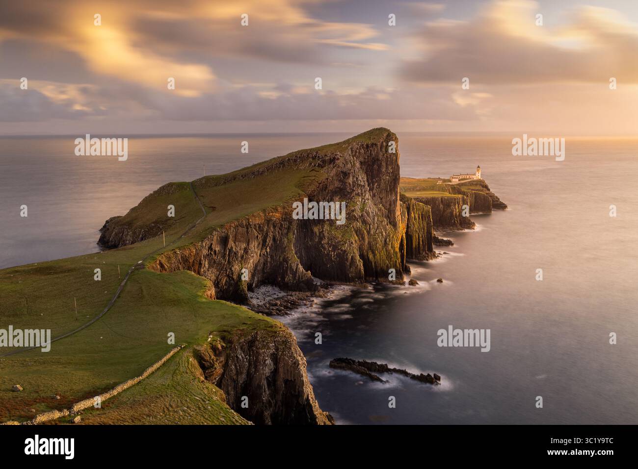 Blick auf die Klippen von neist Point treffen auf das rastlose Meer unter einem mit Gold- und Perltönen bemalten Himmel, ein Leuchtturm steht auf Wächter, Isle of Skye, Schottland, Großbritannien. Stockfoto