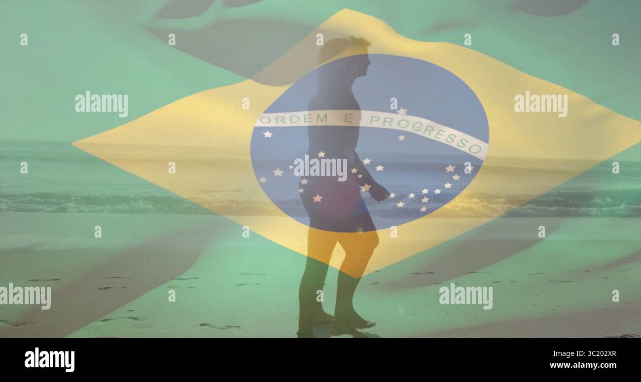 Walking Surfer in Boardshorts mit Surfbrett am Strand bei Ebbe, brasilianische Flagge überlagert Stockfoto