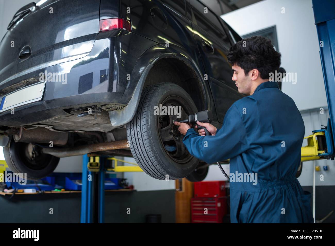 Dunkle Heckklappe, die in der Reparaturwerkstatt auf dem hydraulischen Hubwerk aufsteigt und einen pneumatischen Schlagschrauber am Rad zeigt Stockfoto