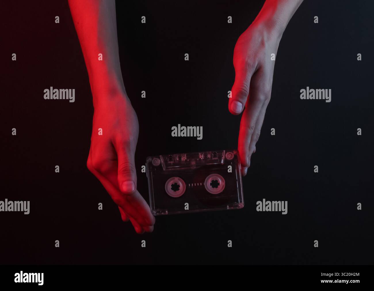 Weibliche Hände halten eine Retro-Audiokassette auf schwarzem Hintergrund mit rotem Neonlicht Stockfoto