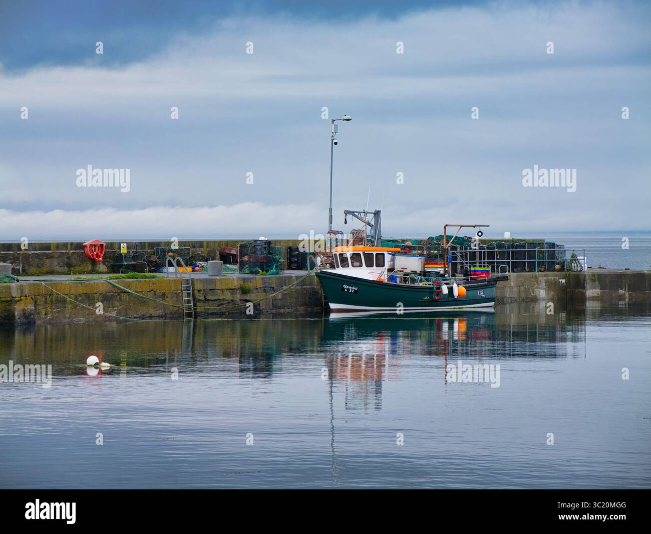 Ballyvaughan, Irland - 12. Juni 2025: Ein Fischerboot ruht ruhig im Hafen von Ballyvaughan, Irland, mit Netzen und Ausrüstung in der Nähe, unter einem bewölkten Himmel. Stockfoto