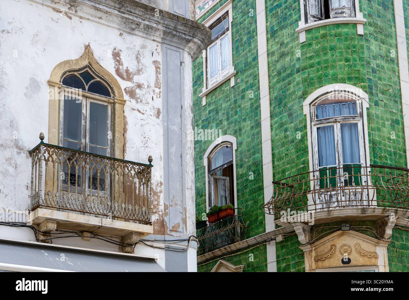 Kontrastierende Gebäudefassaden in Lagos, Portugal, mit einer verwitterten weißen Wand, einem dekorativen Balkon und einem lebhaften, grün gekachelten Gebäude. Stockfoto