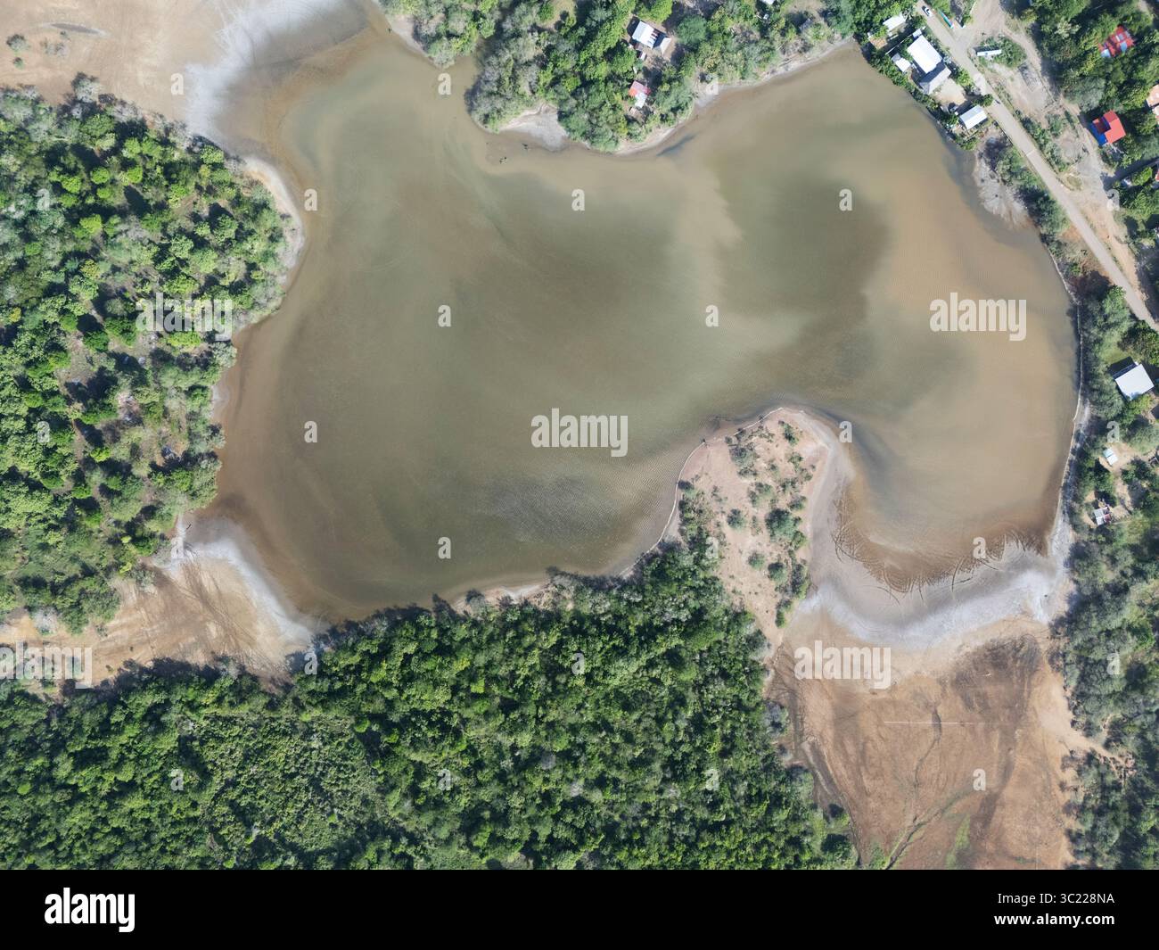 Die weite Luftperspektive zeigt einen sanften Fluss, der sich durch üppige grüne Vegetation unter klarem Himmel schlängelt und eine friedliche Umgebung schafft. Stockfoto