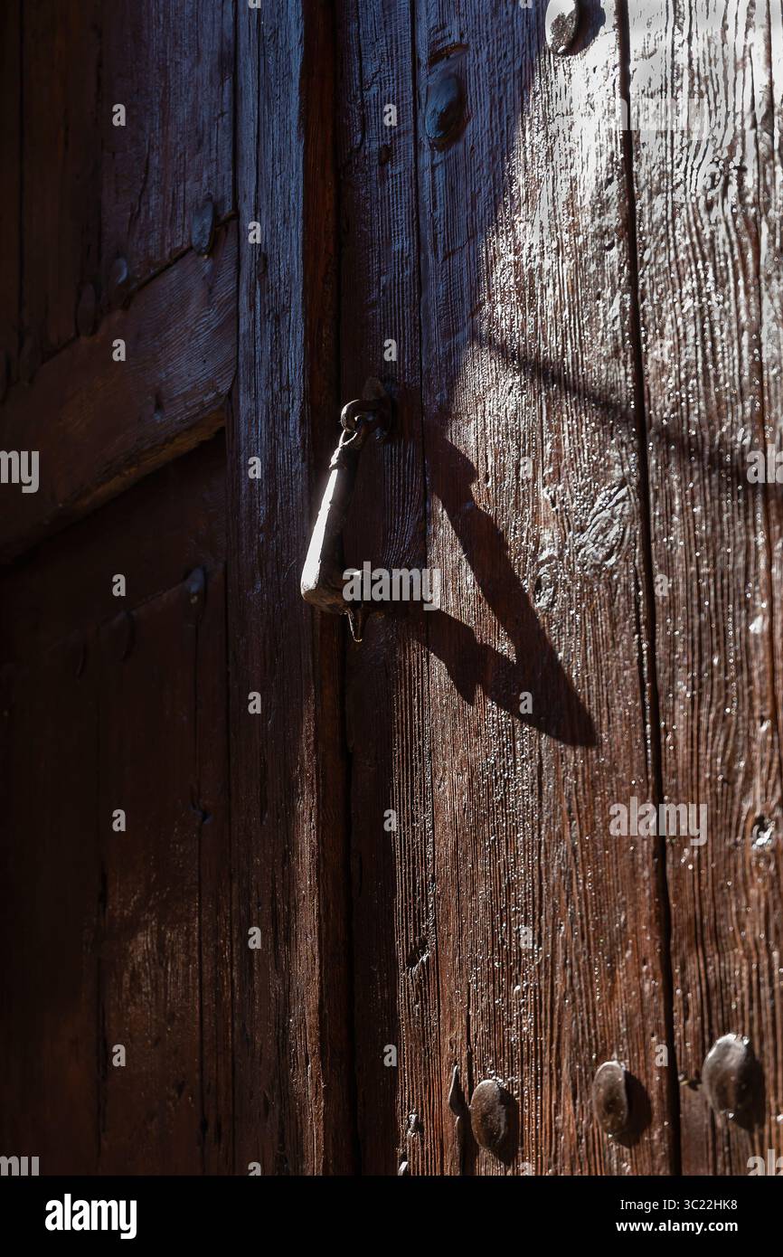 Eine verwitterte Holztür verfügt über einen Vintage-Verschluss, der im warmen Sonnenlicht einen faszinierenden Schatten wirft. Stockfoto