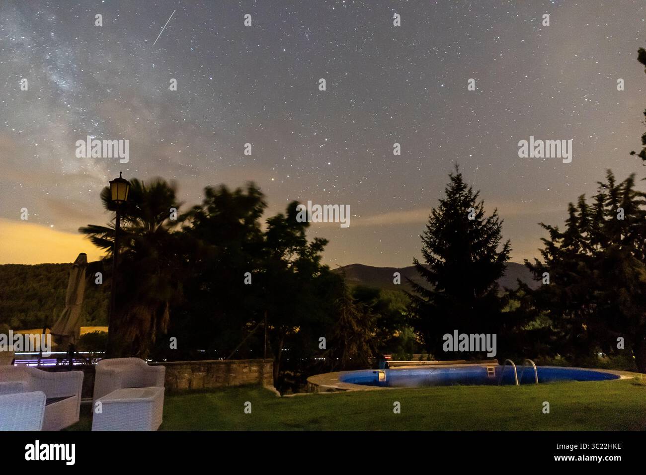 Ein wunderschöner Garten bietet einen glühenden Pool, umgeben von Grün und unter einem Sternenhimmel. Stockfoto