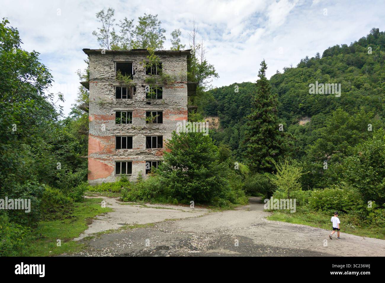 Dramatische Landschaft von Akarmara Stadt, Tkvarcheli Stadt, Abchasien. Altes zerstörtes Gebäude, urbane Ruinen, die im Sommer von grünen Pflanzen bewachsen sind Stockfoto