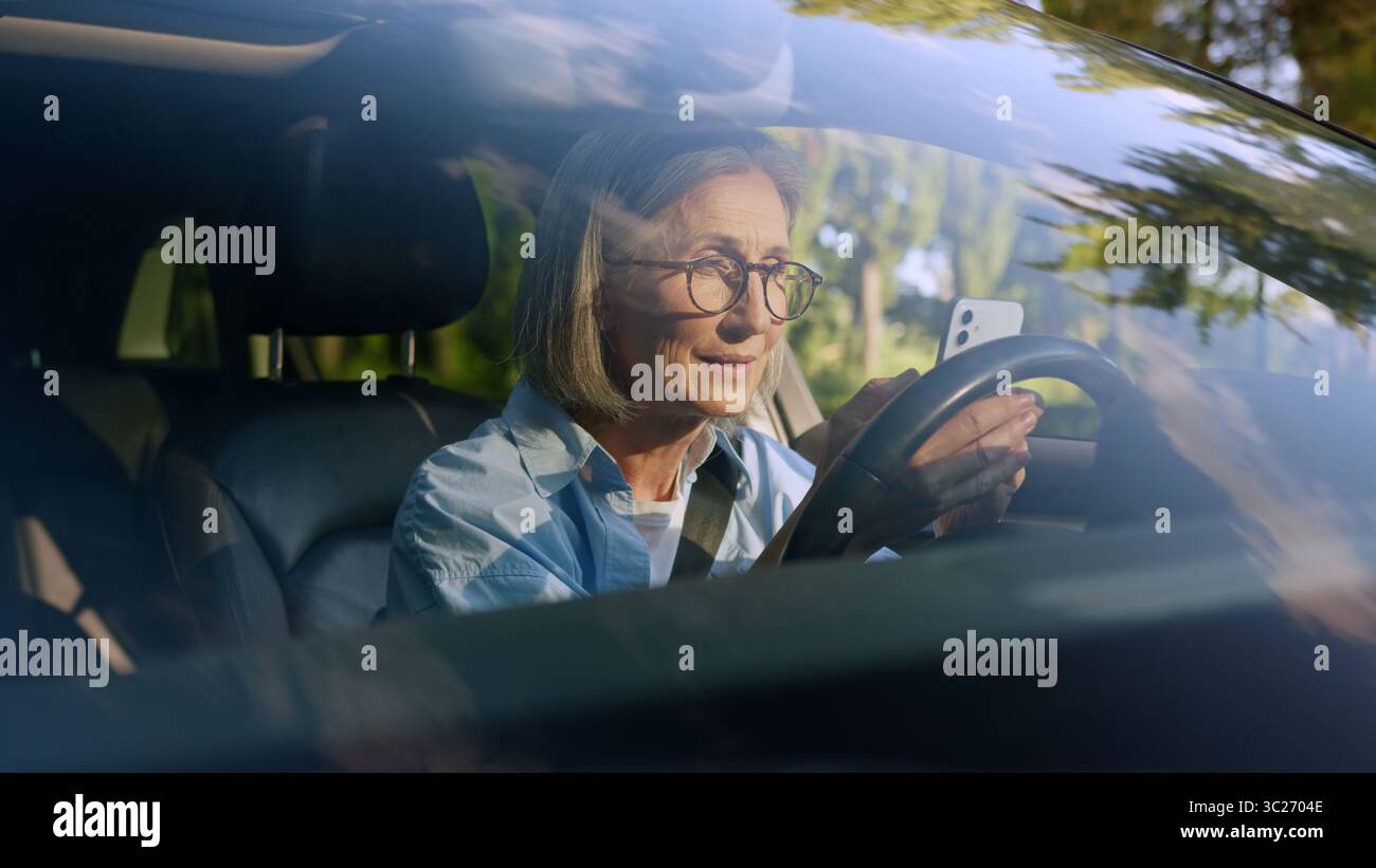 Aufgeregt schockiert überrascht kaukasische ältere ältere Frau weibliche ältere Fahrer Auto Besitzer im Auto mit Handy-App gewinnen lesen großartig Stockfoto