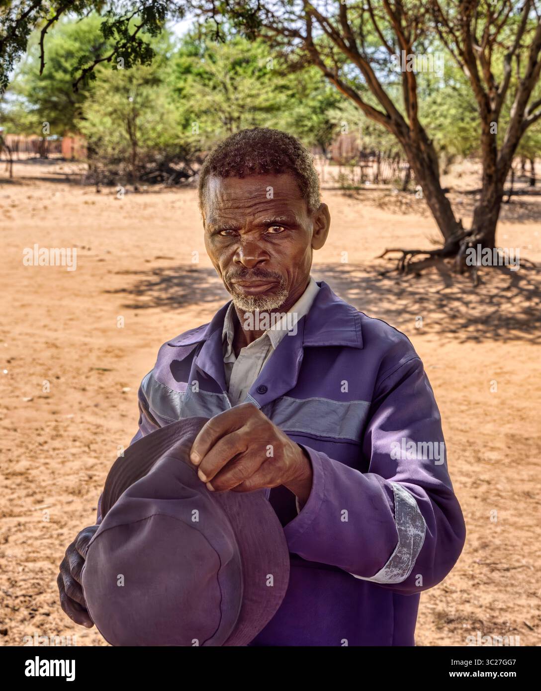Porträt einzelner alter afrikanischer Mann im Afrika-Dorf, Arbeitskleidung, mit einem Eimerhut, Stockfoto