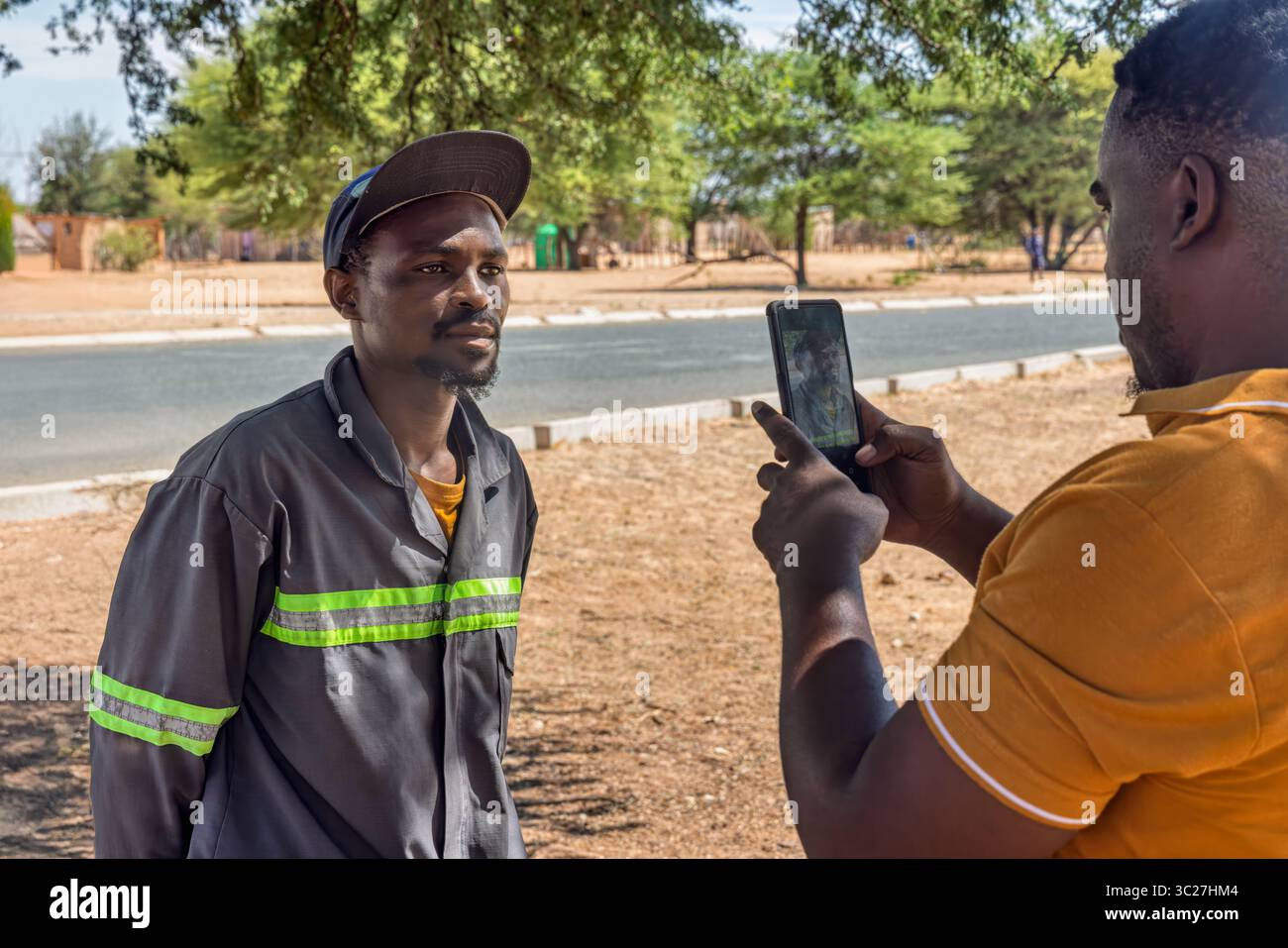 afrikanisches Dorf, zwei Mann draußen, die ein Telefon benutzen, melden sich freiwillig bei der Wohltätigkeitsorganisation und machen Fotos von den Dorfbewohnern in der Gemeinde Stockfoto