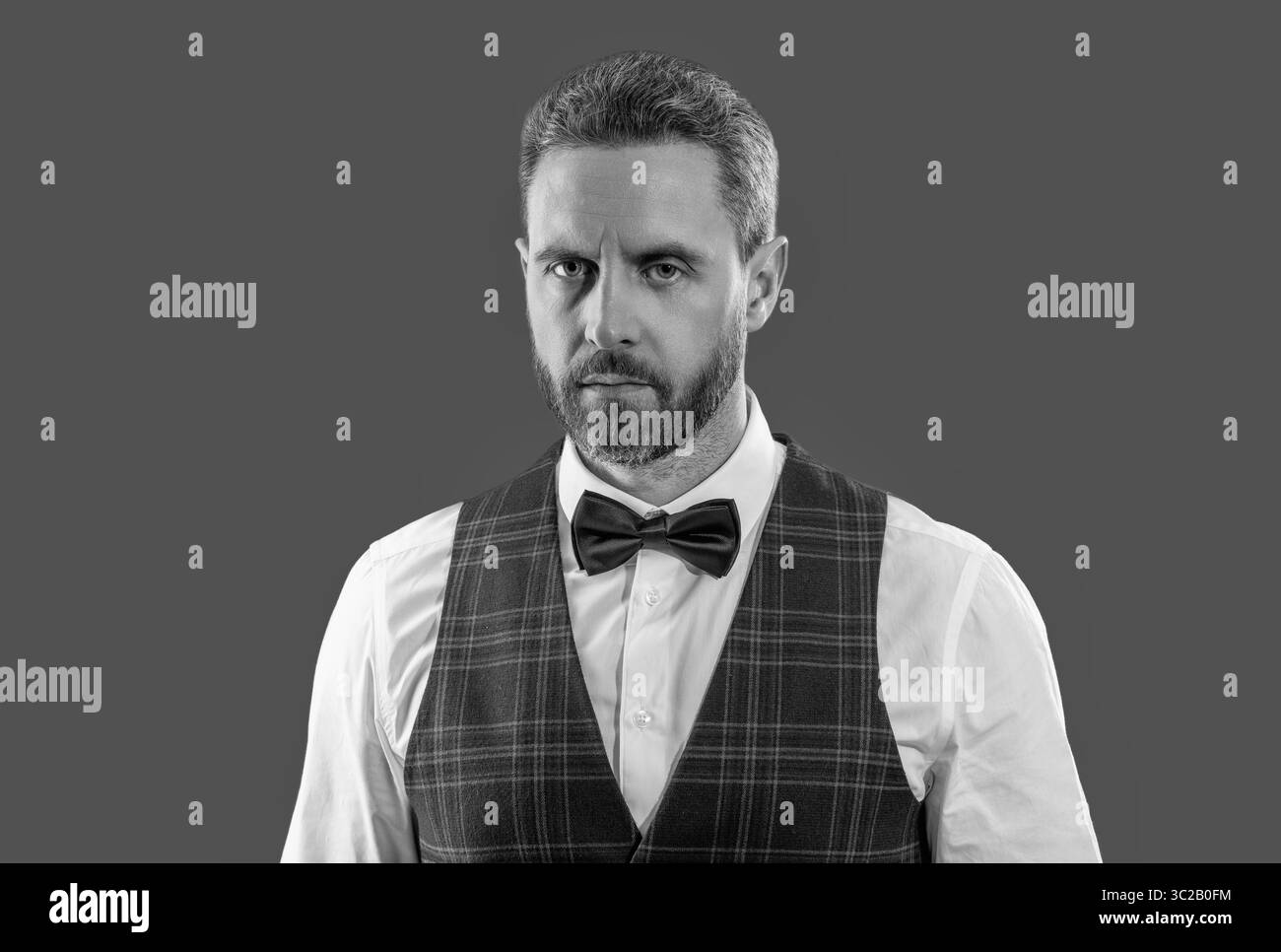 Hübscher charismatischer Kellner trägt elegante Bugtie in klassischer Uniform, isoliert auf Grau Stockfoto