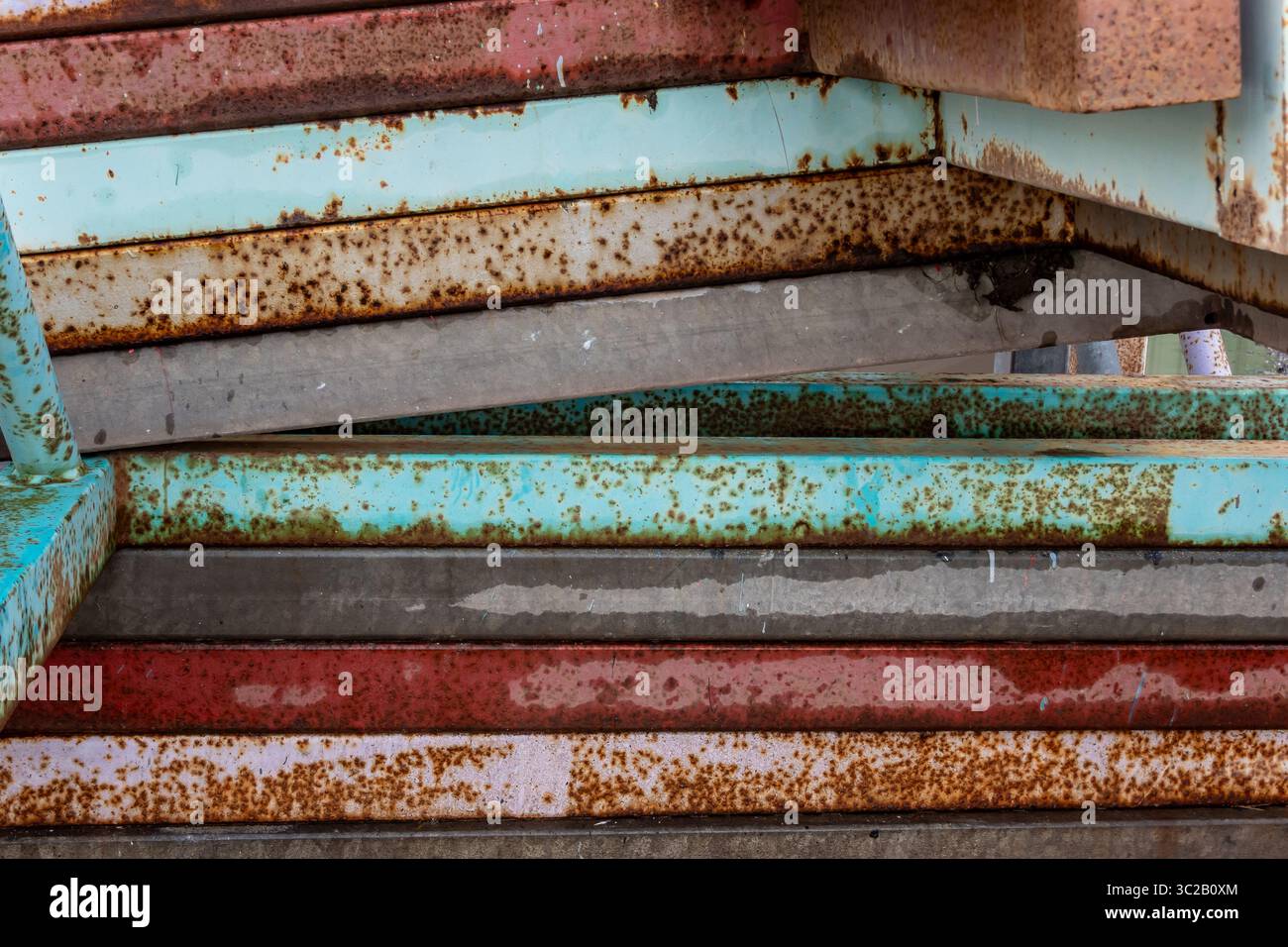 Rostige Metallbalken stapeln sich zusammen und zeigen Alter und Witterungseinflüsse. Abblätternde Farbe in verschiedenen Farben und Rostflecken erzeugen eine strukturierte Oberfläche Stockfoto