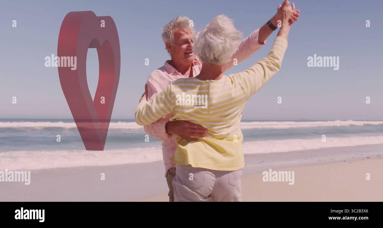 Tanzendes Seniorenpaar, das die Hände erhebt, umarmt am Sandstrand am Meer, mit rotem Herz Stockfoto