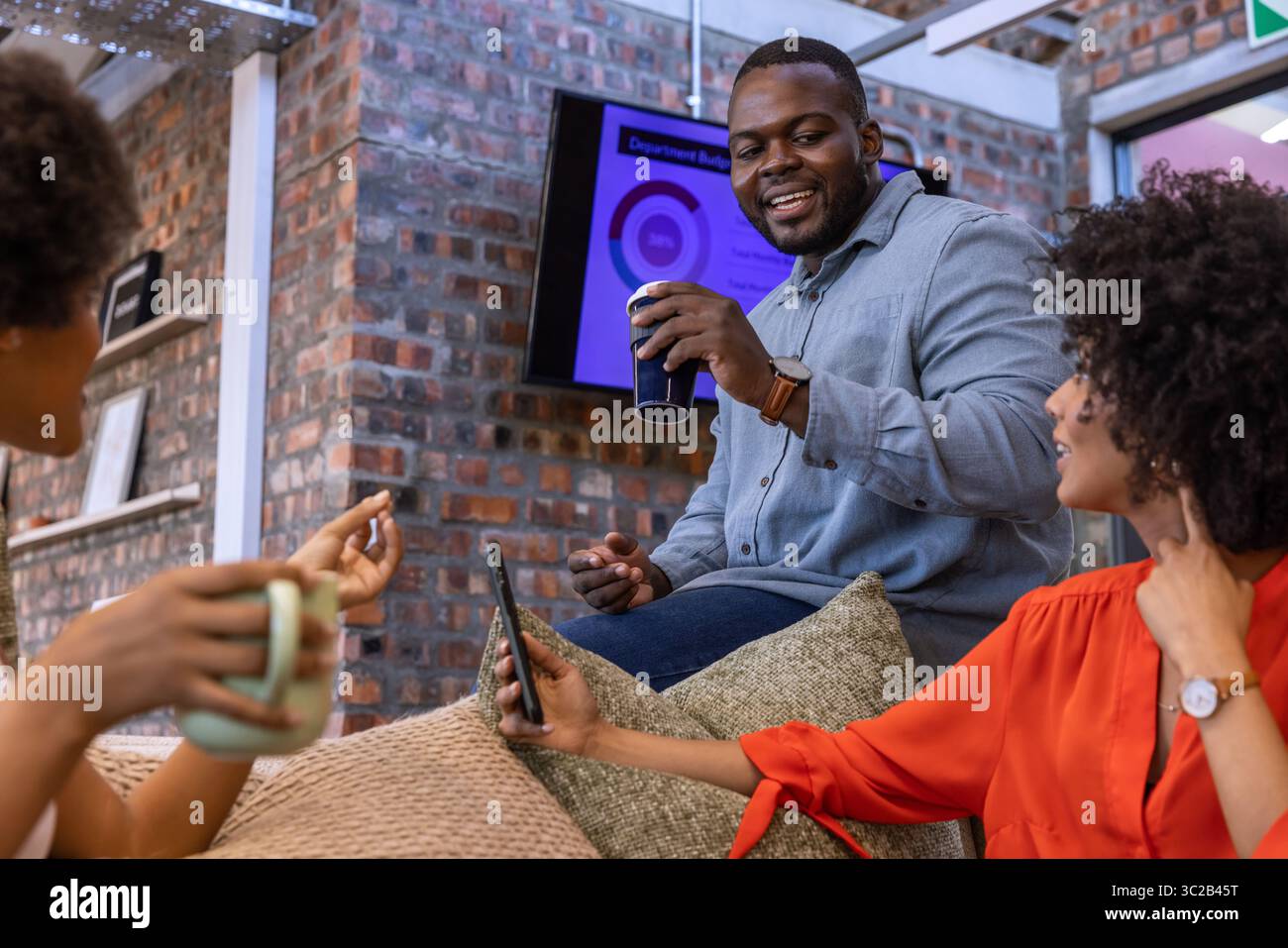 Verschiedene Kollegen diskutieren Karten auf dem Bildschirm, während sie den Reisebecher in der Bürolounge halten Stockfoto