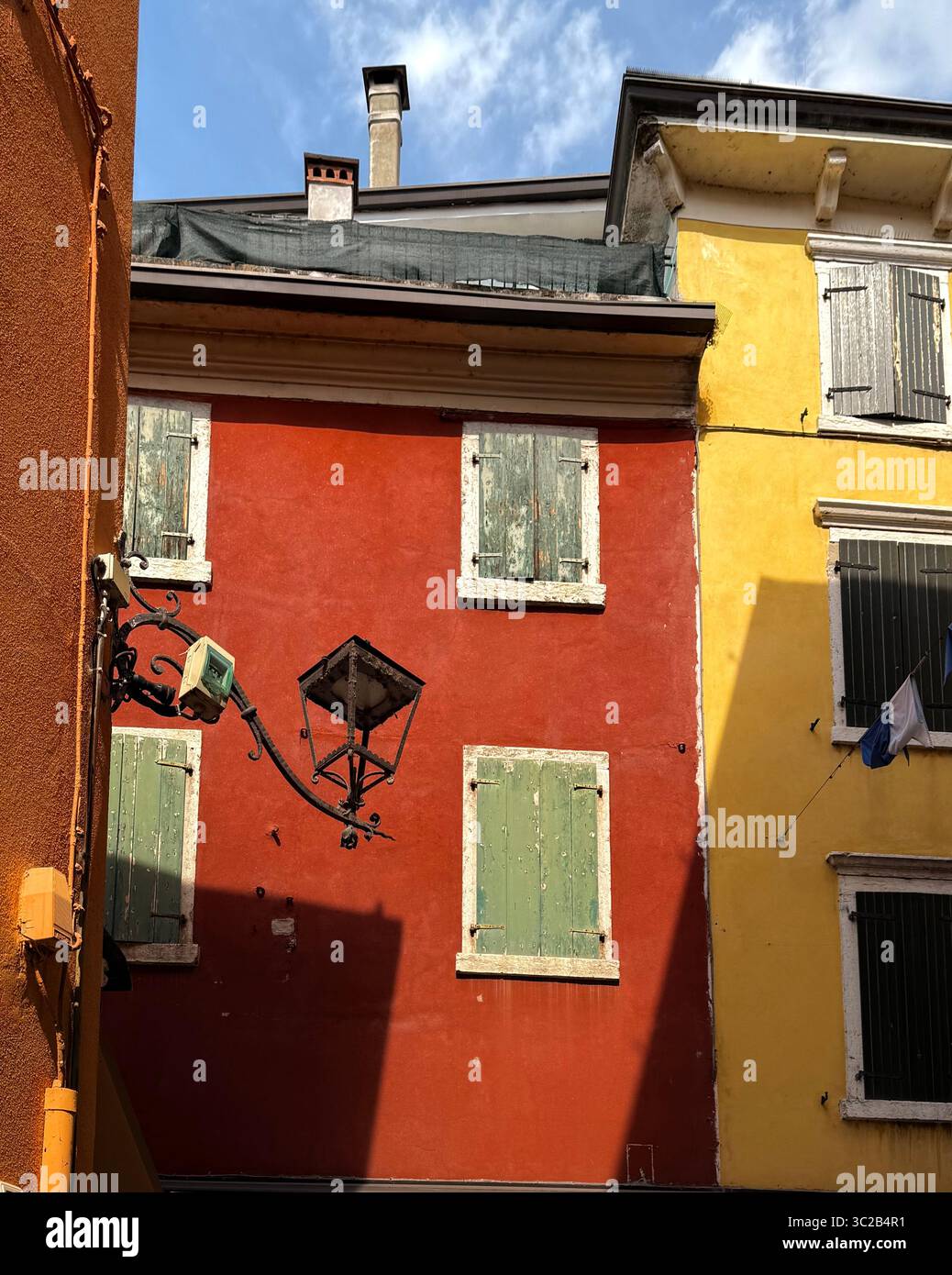 Rote Wand und grüne Fensterläden mit Lampe in Garda, Italien Stockfoto