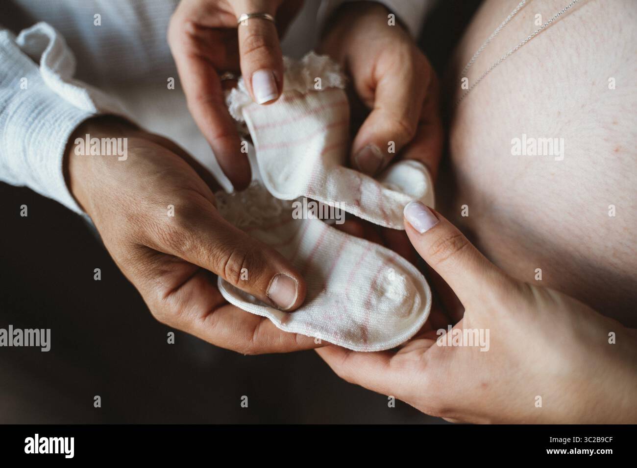 Die Hände werdender Eltern halten kleine Babysocken sanft und symbolisieren die Liebe und Erwartung für ein neues Familienmitglied. Der intime Moment fängt Jo ein Stockfoto