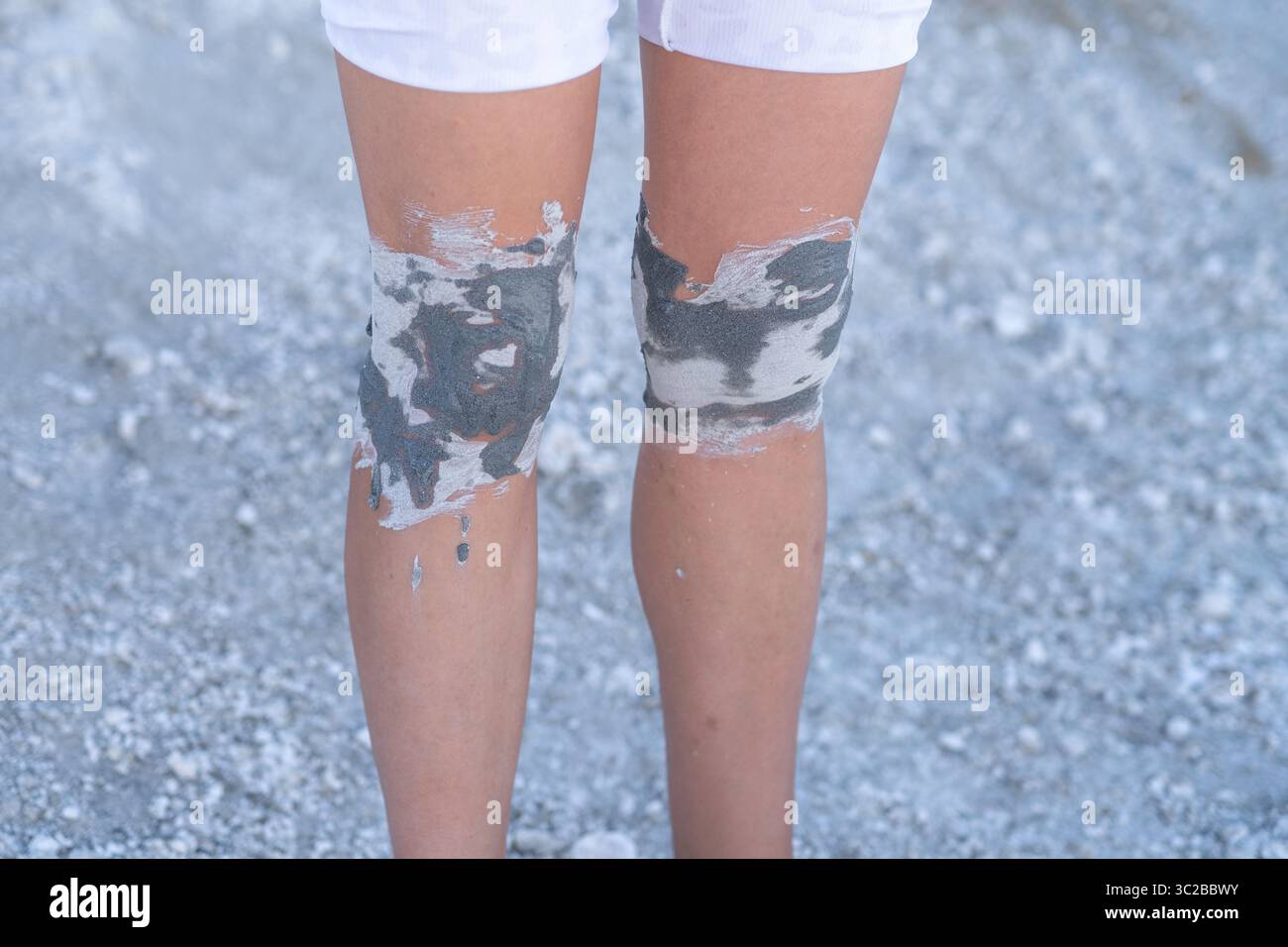 Person mit bemalten Knien, die während des Sonnentages im Freien auf hellem Kies steht und Kreativität und künstlerischen Ausdruck zeigt Stockfoto