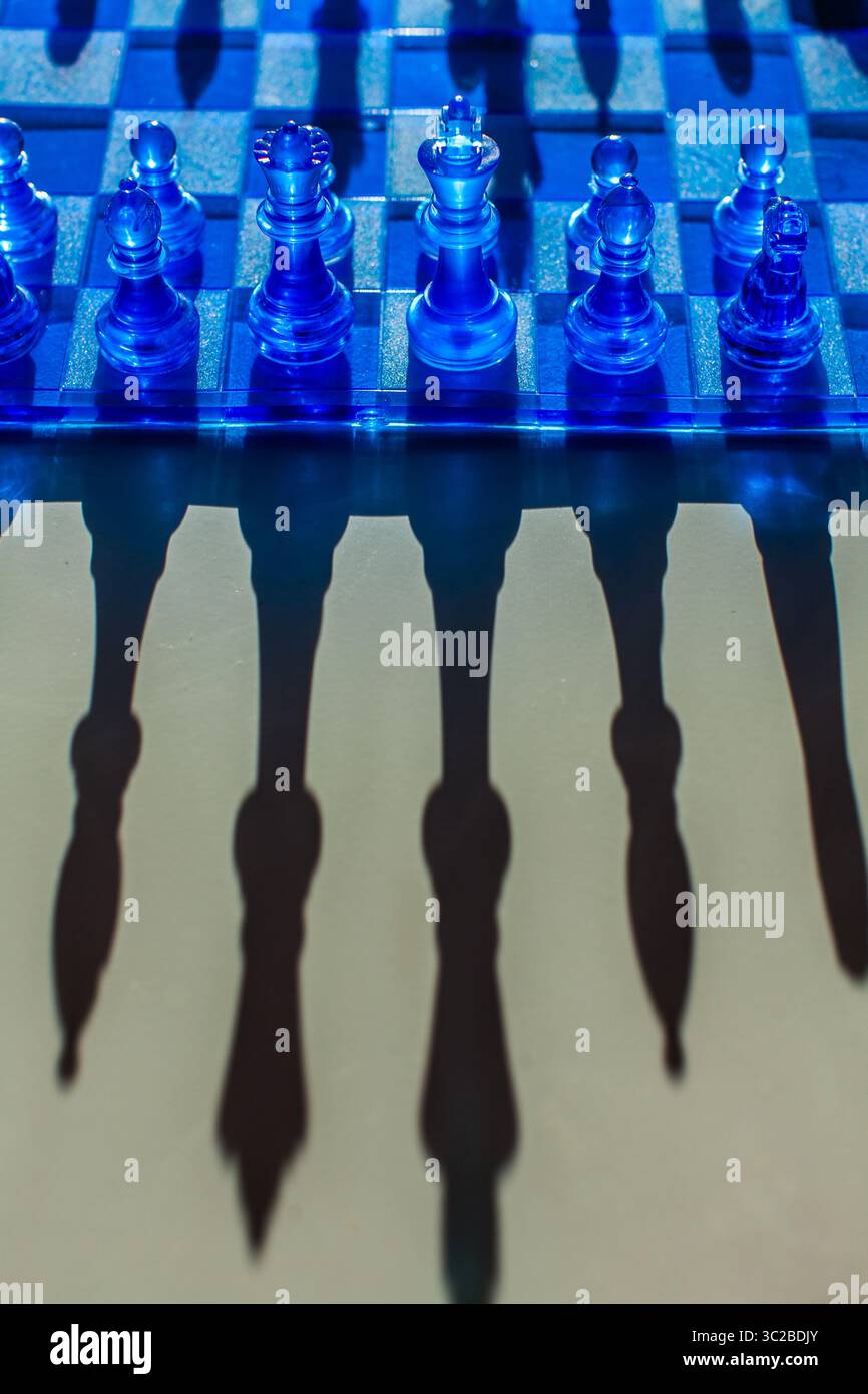 Ein faszinierendes Schachbrett mit durchscheinenden blauen Teilen wirft dramatische Schatten und schafft eine visuell eindrucksvolle und strategische Szene Stockfoto