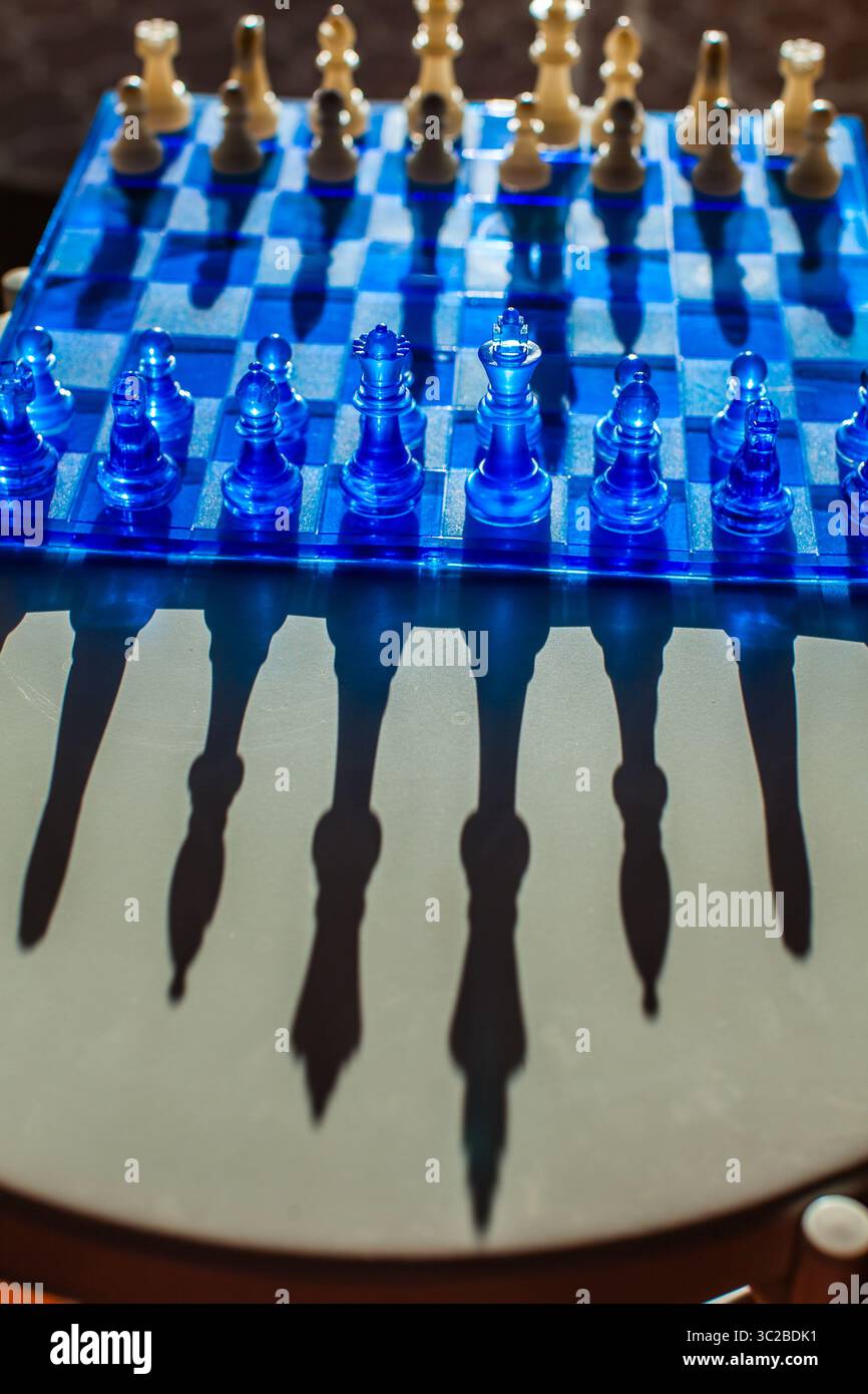 Ein faszinierendes Schachbrett mit durchscheinenden blauen Teilen wirft dramatische Schatten und schafft eine visuell eindrucksvolle und strategische Szene Stockfoto