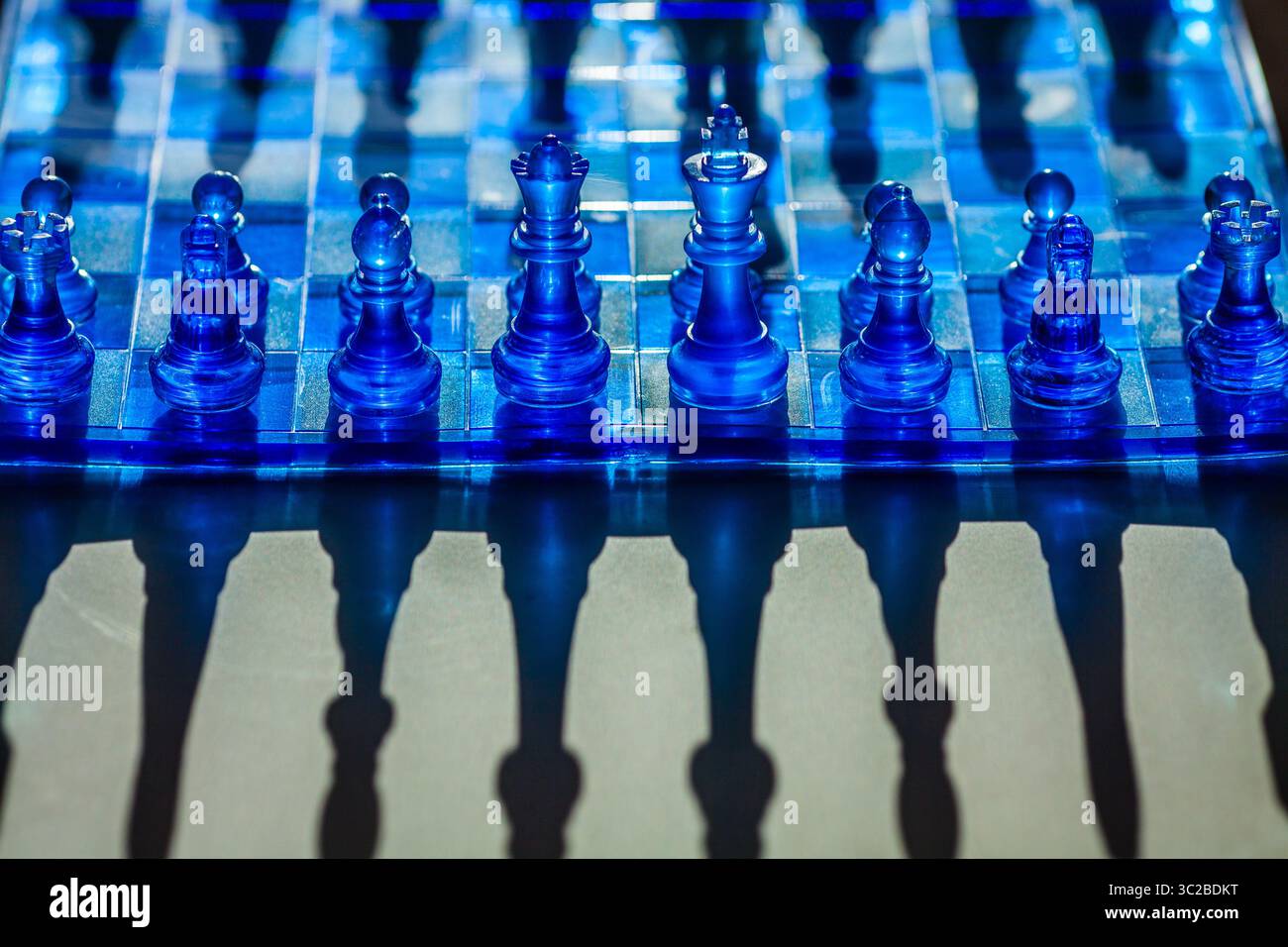 Ein faszinierendes Schachbrett mit durchscheinenden blauen Teilen wirft dramatische Schatten und schafft eine visuell eindrucksvolle und strategische Szene Stockfoto