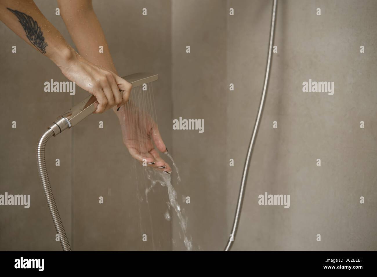 Die Hände werden unter fließendem Wasser aus einem eleganten Duschkopf in einem stilvollen Badezimmer positioniert. Die Einrichtung verfügt über klare Linien und neutrale Wände, betont Stockfoto