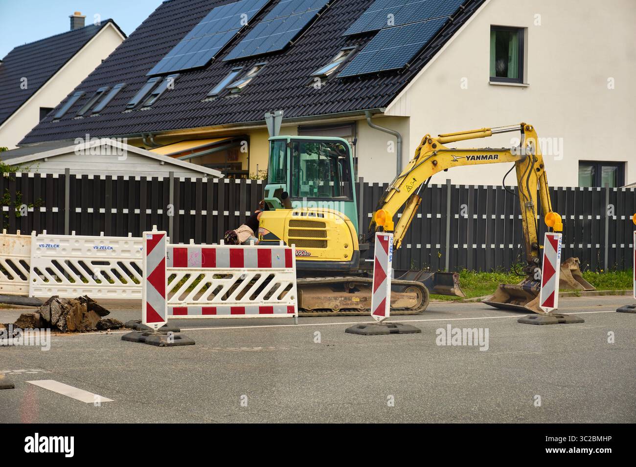 16. Juli 2025 – Sievershagen-Deutschland: Wochenendbauszene mit inaktivem Minibagger, Sicherheitsbarrieren und Schildern in einem Wohngebiet mit Solarenergie Stockfoto