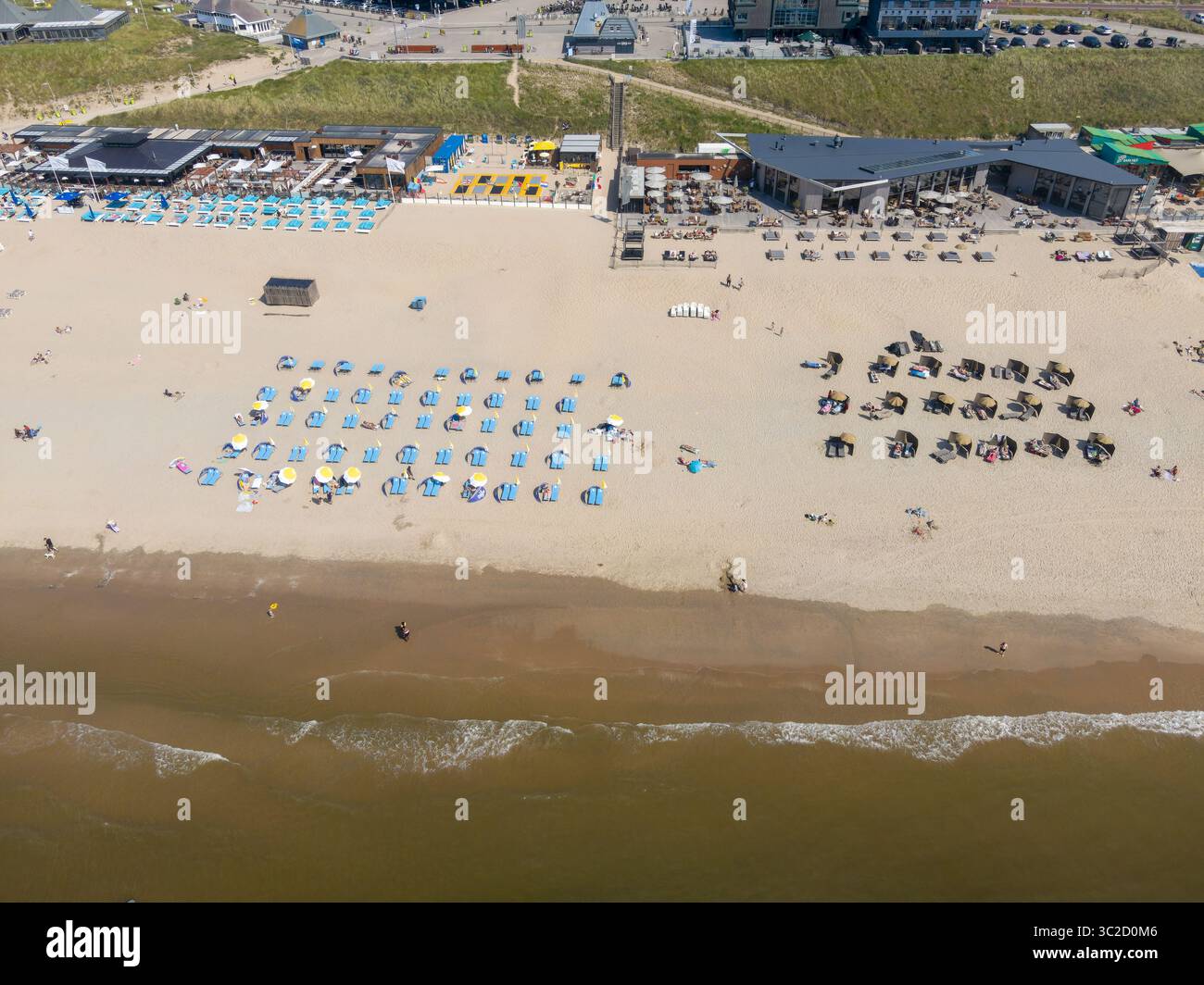 Aus der Vogelperspektive auf den Sandstrand mit farbenfrohen Sonnenschirmen und Sonnenanbetern, die auf die rhythmischen Wellen der Nordsee treffen, Zandvoort, Nordholland, Niederlande. Stockfoto