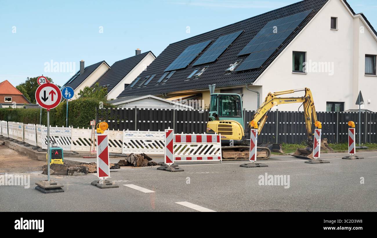 16. Juli 2025 – Sievershagen-Deutschland: Wochenendbauszene mit inaktivem Minibagger, Sicherheitsbarrieren und Schildern in einem Wohngebiet mit Solarenergie Stockfoto