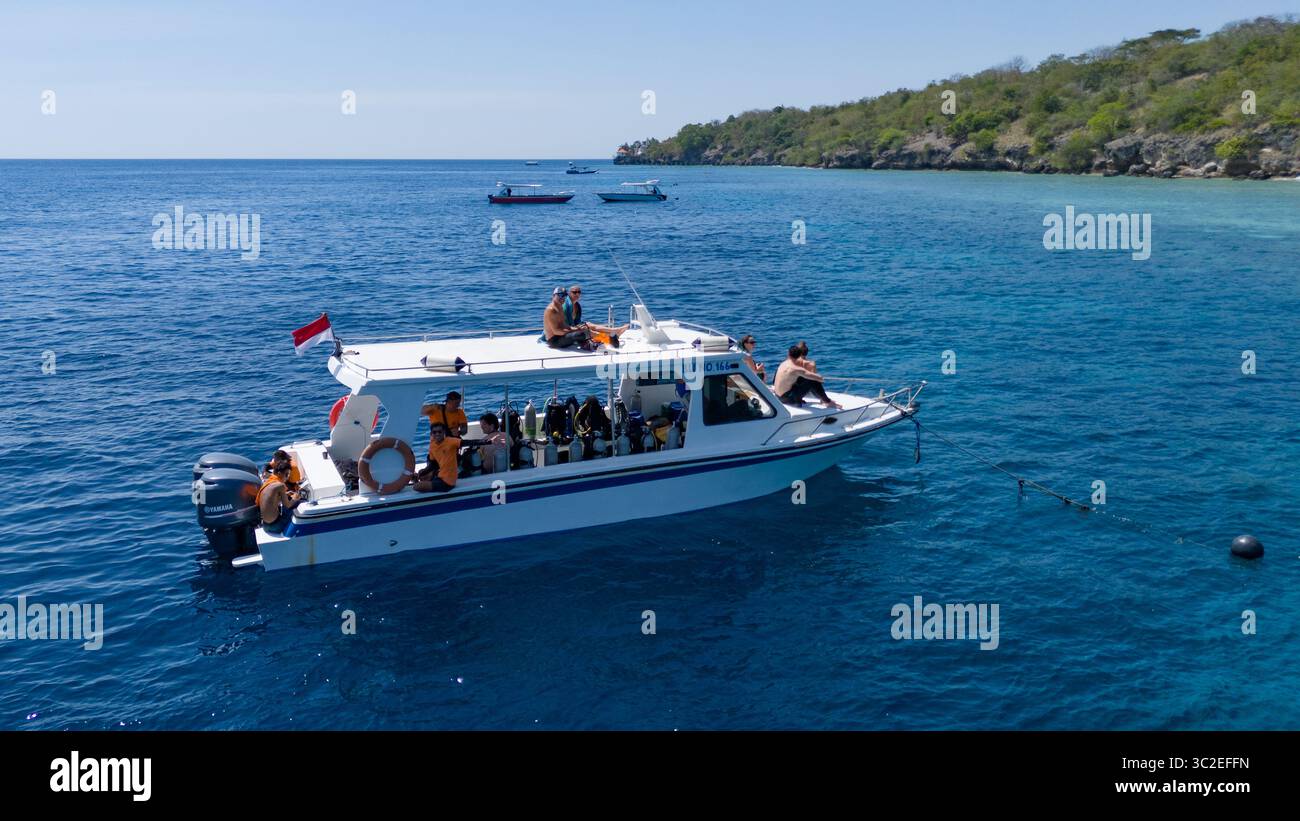 Pemuteran, Indonesien - 22. August 2024: Aus der Vogelperspektive eines weißen Bootes, das durch das braune Meer fährt, Taucher, die sich vor dem Hintergrund der üppigen Küste Balis vorbereiten. Stockfoto