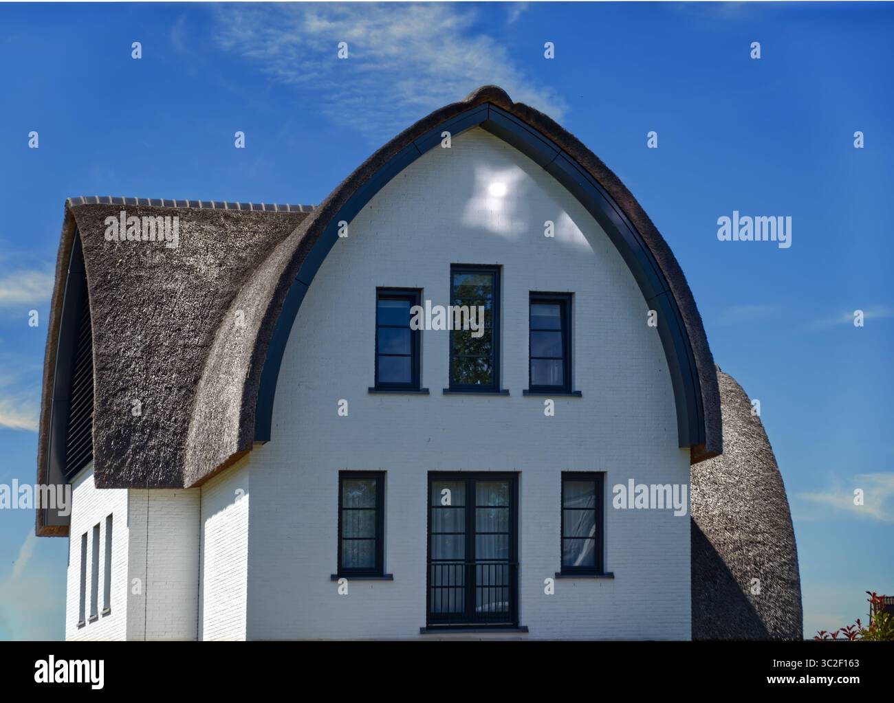 Weißes modernes Haus mit traditionellem Strohdach unter blauem Himmel, das umweltfreundliche Baupraktiken und nachhaltiges Wohnen demonstriert Stockfoto