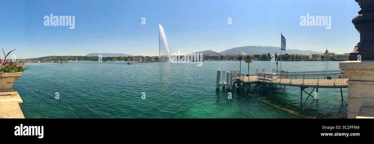 Breites Panoramabild mit einem See mit einem hoch aufragenden Wasserbrunnen, einem Dock und einer malerischen städtischen Umgebung. Ideal für Hintergründe, Header oder Stockfoto