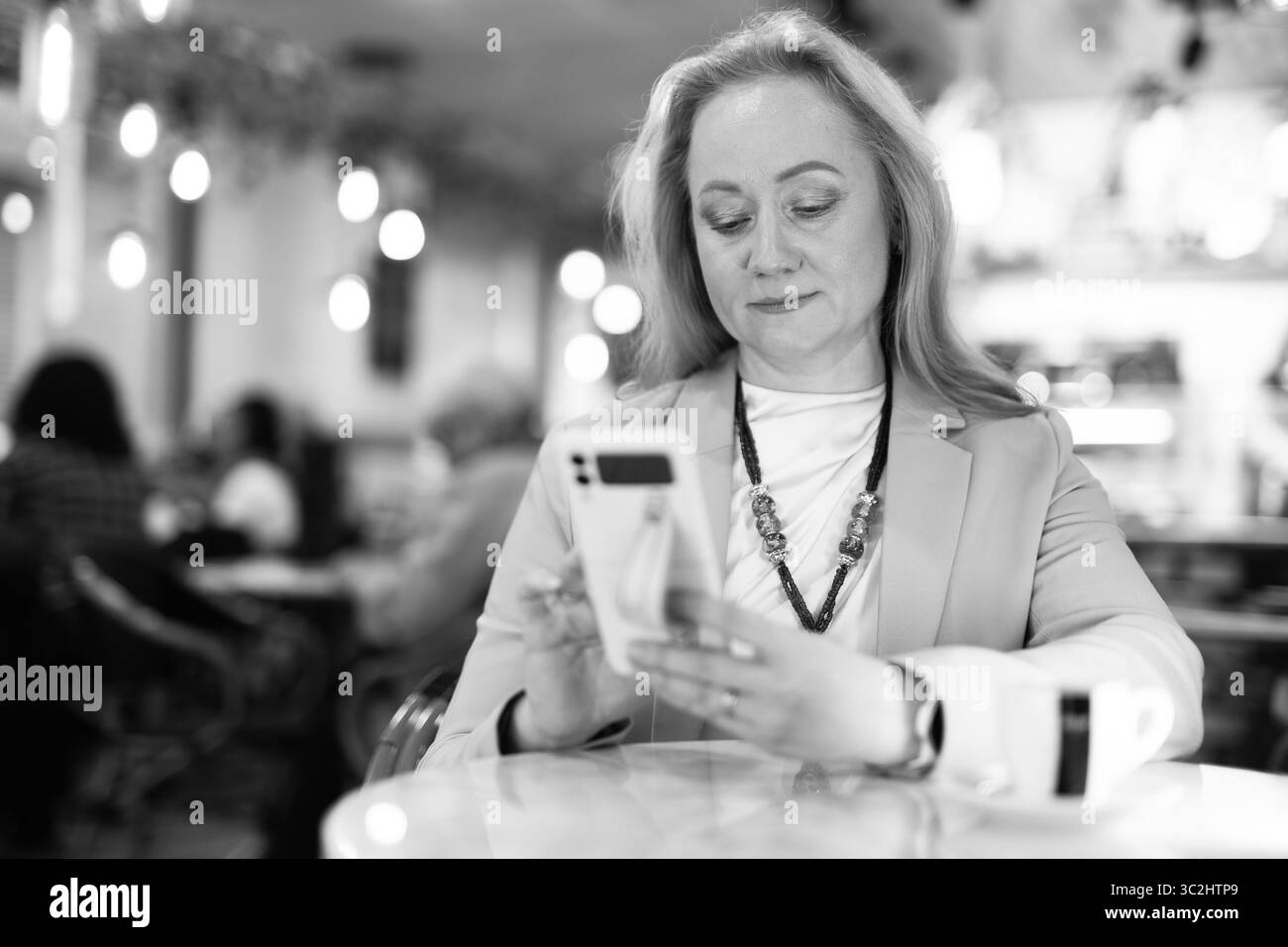 Frau sitzt am Tisch im Restaurant, trinkt Kaffee und schreibt eine Nachricht am Telefon. Stockfoto