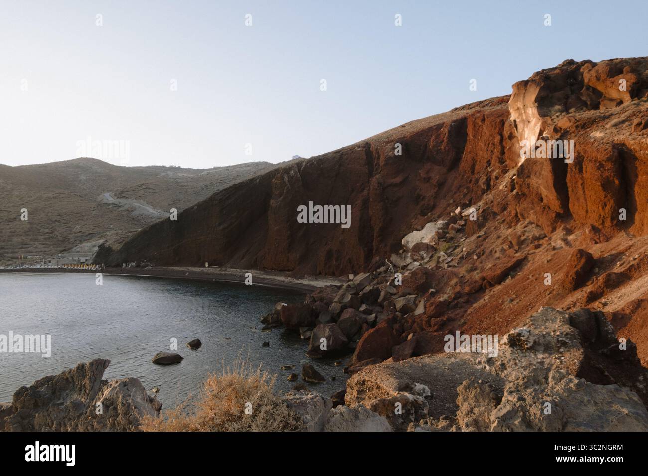 Roter Strand in Santorin, Griechenland, bei Sonnenuntergang in Akrotiri gefangen, mit markanten roten Klippen, blauem Wasser, vulkanischem Sand und großen Felsen Stockfoto