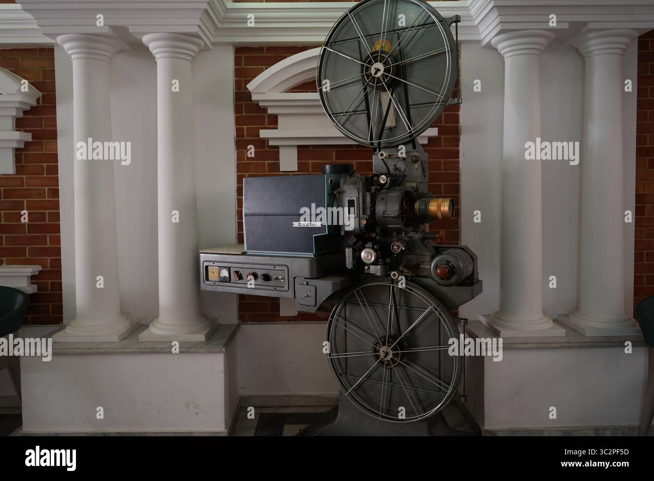 Ein klassischer 35-mm-Filmprojektor CX 21H in einem Kino im Vintage-Stil, umgeben von Säulen und roten Backsteinen, repräsentiert Retro-Filmtechnologie Stockfoto