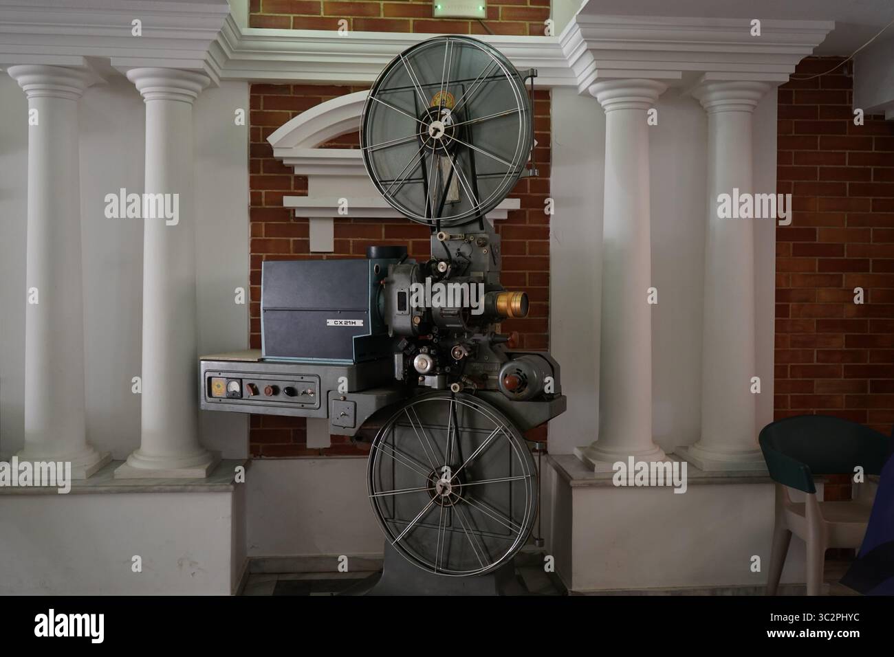 Ein klassischer 35-mm-Filmprojektor CX 21H in einem Kino im Vintage-Stil, umgeben von Säulen und roten Backsteinen, repräsentiert Retro-Filmtechnologie Stockfoto