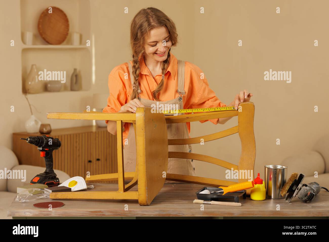 Frau restauriert Holzstuhl, mit Werkzeugen für Reparaturen, kreatives Renovierungsprojekt in der Heimwerkstatt. Stockfoto