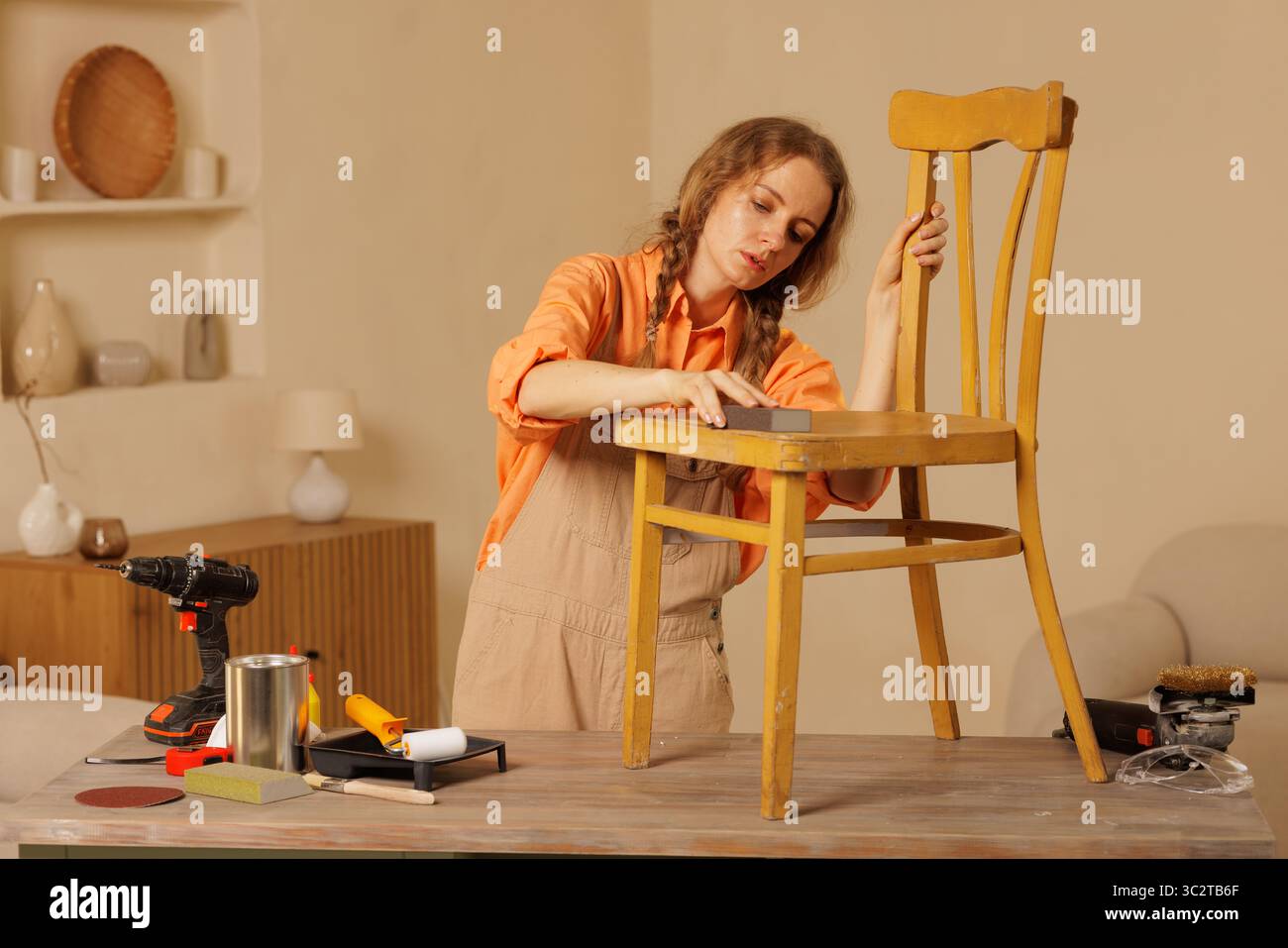 Frau schleift Vintage-Stuhl vor dem Umlackieren, Restaurierungsprozess, kreatives Heimwerkerprojekt. Stockfoto