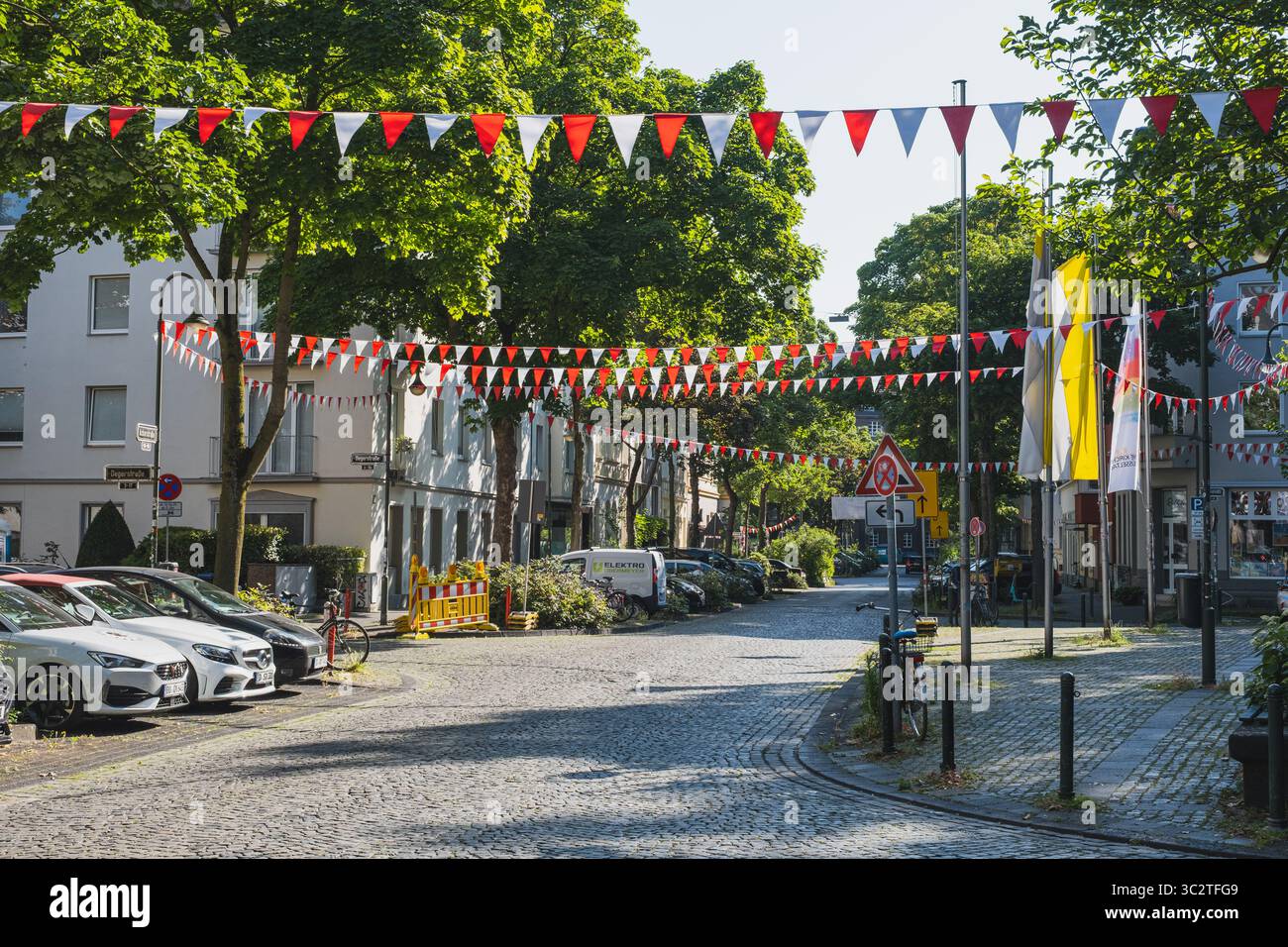 Sonnige Kopfsteinpflasterstraße mit festlichen rot-weißen Fahnen Stockfoto Sonnige Kopfsteinpflasterstraße mit festlichen rot-weißen Fahnen Stockfoto