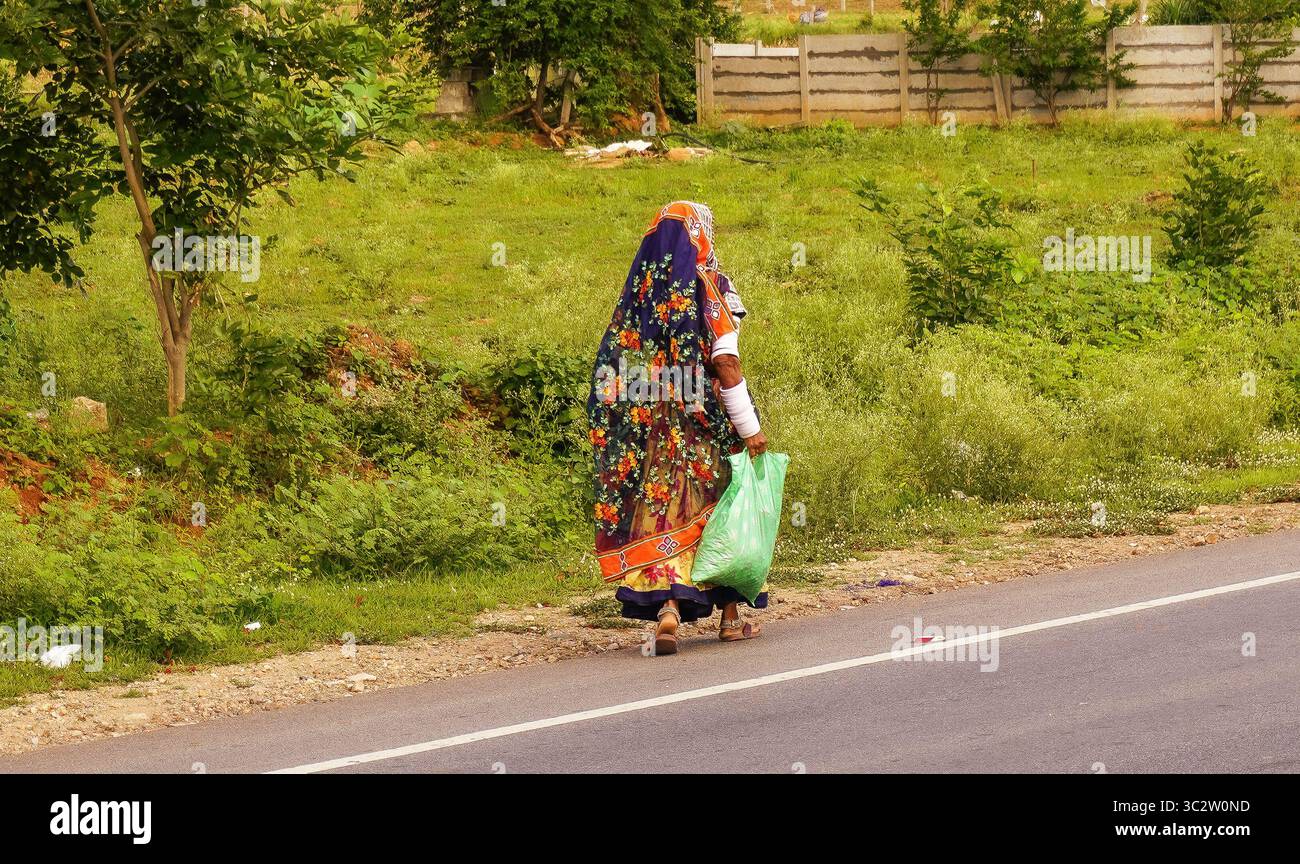Lambadi Banjaaran Frau, die in traditioneller Kleidung entlang der Landstraße spaziert Stockfoto