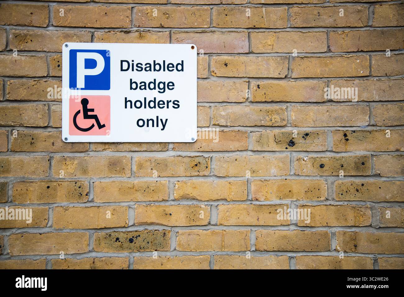 Nur für Behindertenausweishalter ist ein an einer Ziegelwand angebrachtes Parkschild mit Hinweis auf eingeschränkte Parkmöglichkeiten für Inhaber blauer Ausweisschilder in einem ausgewiesenen Bereich. Stockfoto