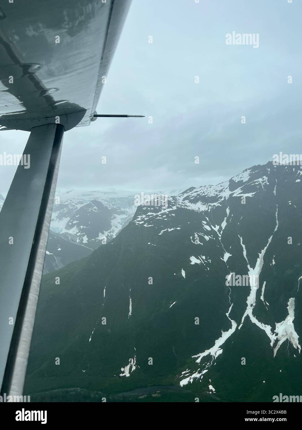 Aus der Vogelperspektive über schneebedeckte Berge und Wälder auf dem Weg zum Lake Clark National Park, Alaska. Reise durch die wilde Wildnis Alaskas - Smartphone-aufgenommenes Stockfoto