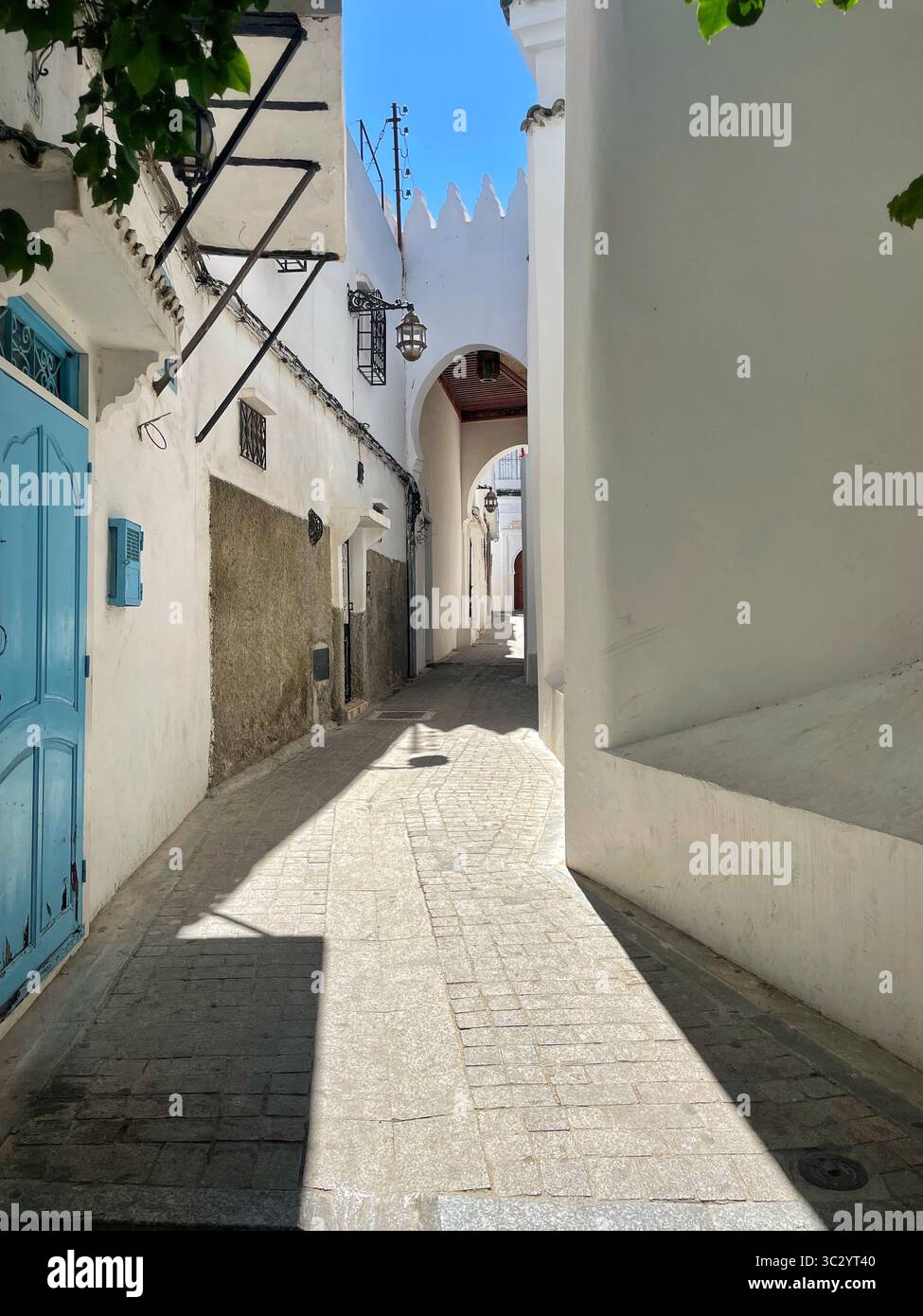 Enge Gasse in der Medina von Tanger. Sonnenlicht, das die weiß getünchten Wände durchzieht, ein ruhiger Durchgang unter dem alten Stadttor. Juni 2024. Stockfoto