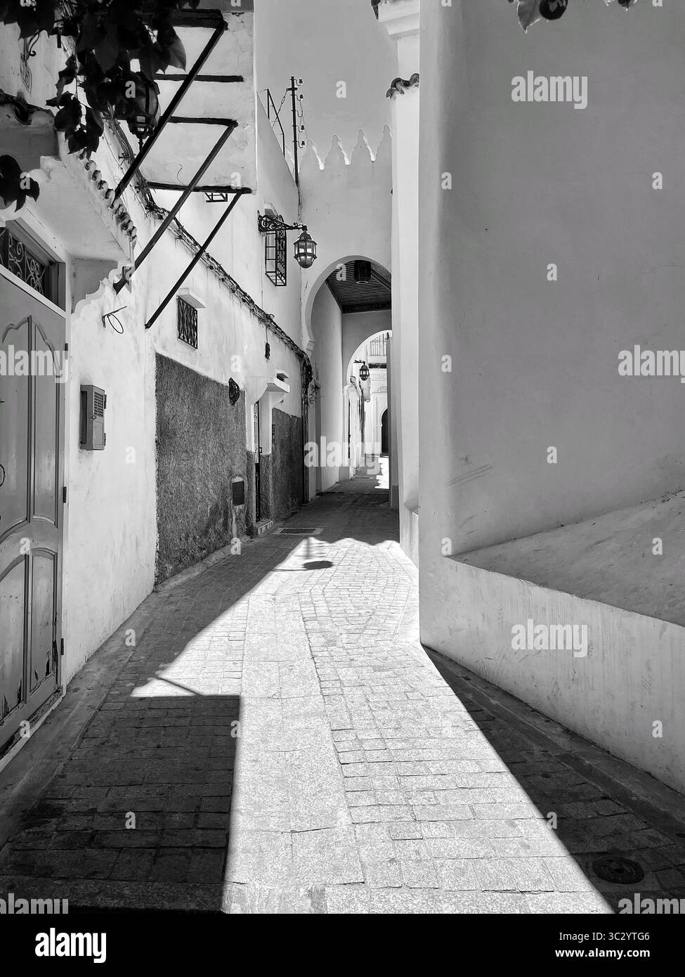 Enge Gasse in der Medina von Tanger. Sonnenlicht, das die weiß getünchten Wände durchzieht, ein ruhiger Durchgang unter dem alten Stadttor. Juni 2024. Stockfoto