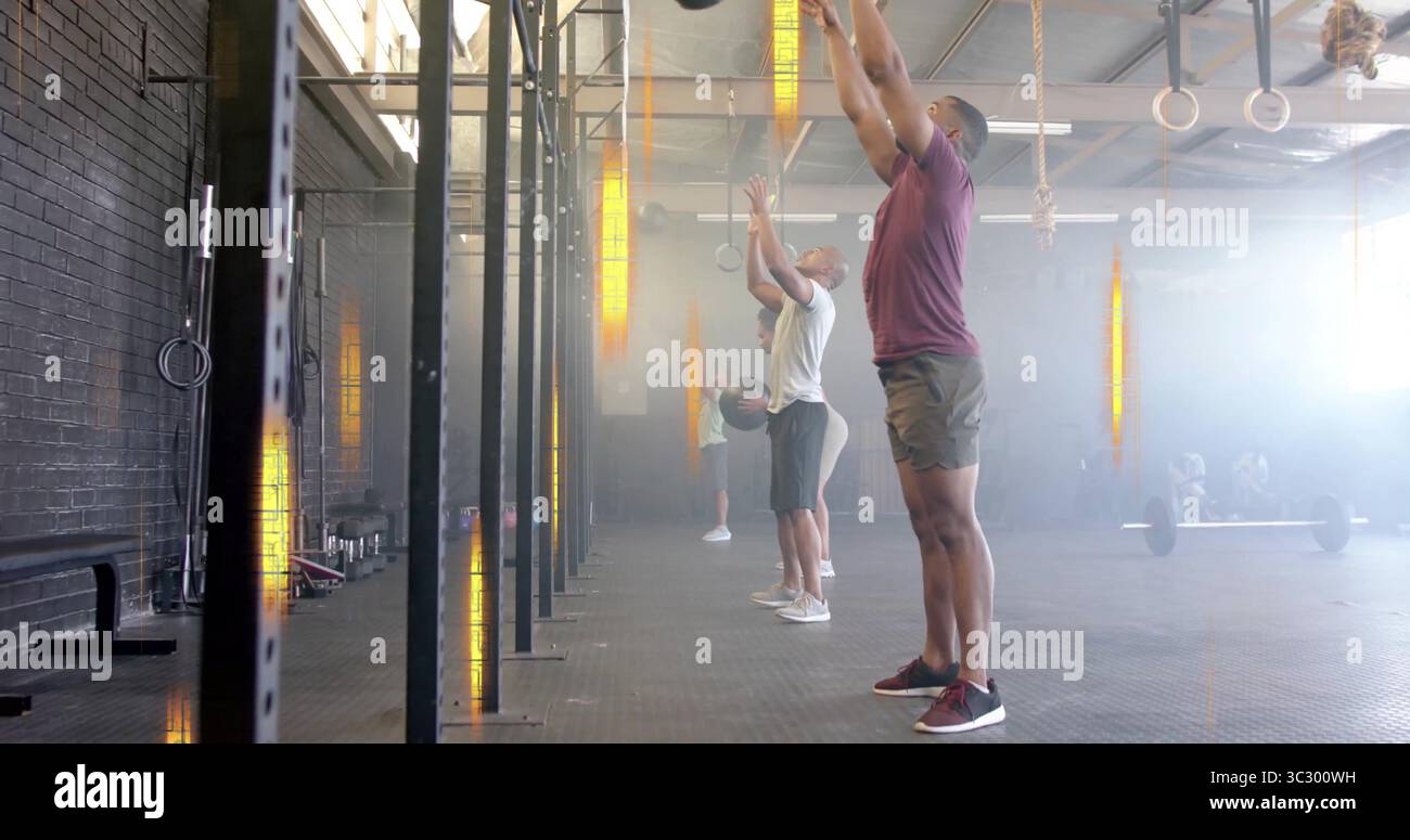 Arbeiten vier Leute in Turnkleidung, werfen über dem Kopf Medizinbälle in Fitness Gym, mit Rigs Stockfoto