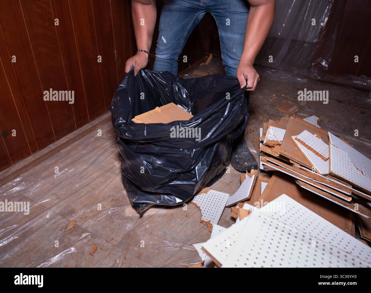 Ein Mann mit einem großen schwarzen Müllsack gefüllt mit kaputten Dachmaterialien während eines Dachersatzprojekts. Ideal zur Illustration von Bauarbeiten Stockfoto