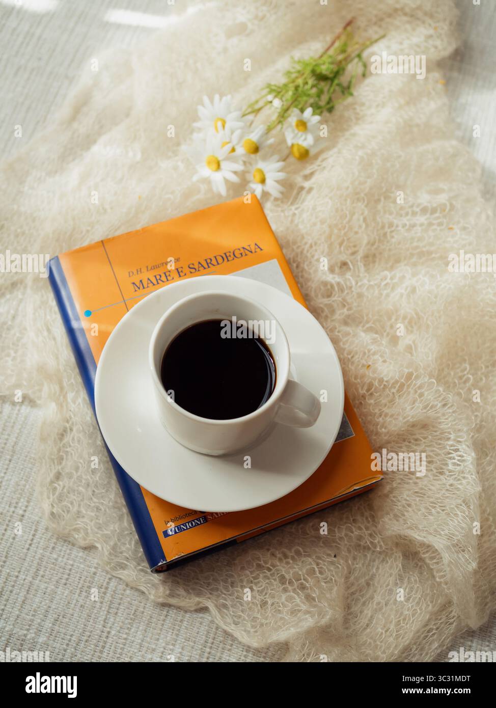 Kaffee auf italienischer Ausgabe von „Meer und Sardinien“ von D.H. Lawrence mit Daisies auf weißem Kaschmir-Schal Stockfoto