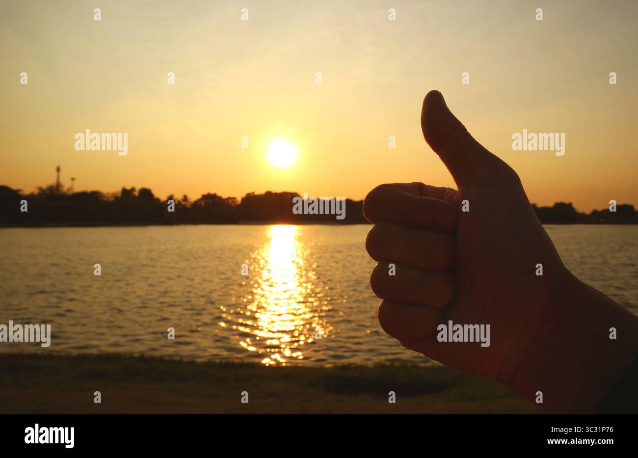 Die Silhouette der Daumen zeigt die aufgehende Sonne über dem See Stockfoto