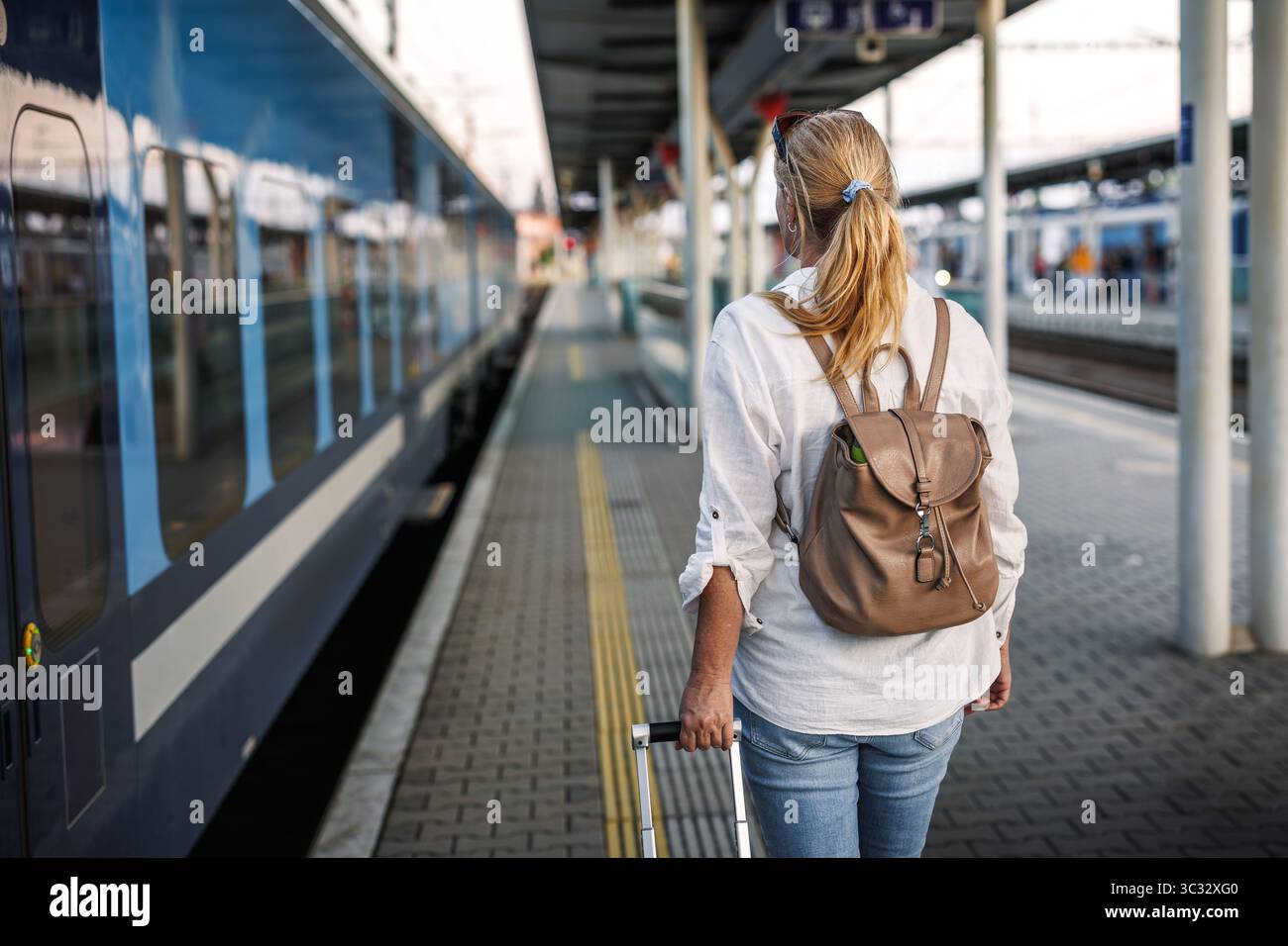 Touristen, die mit dem Zug reisen. Frau mit Rucksack und Koffer, die am Bahnsteig in den Zug einsteigen geht. Alleinreisender Lifestyle Stockfoto