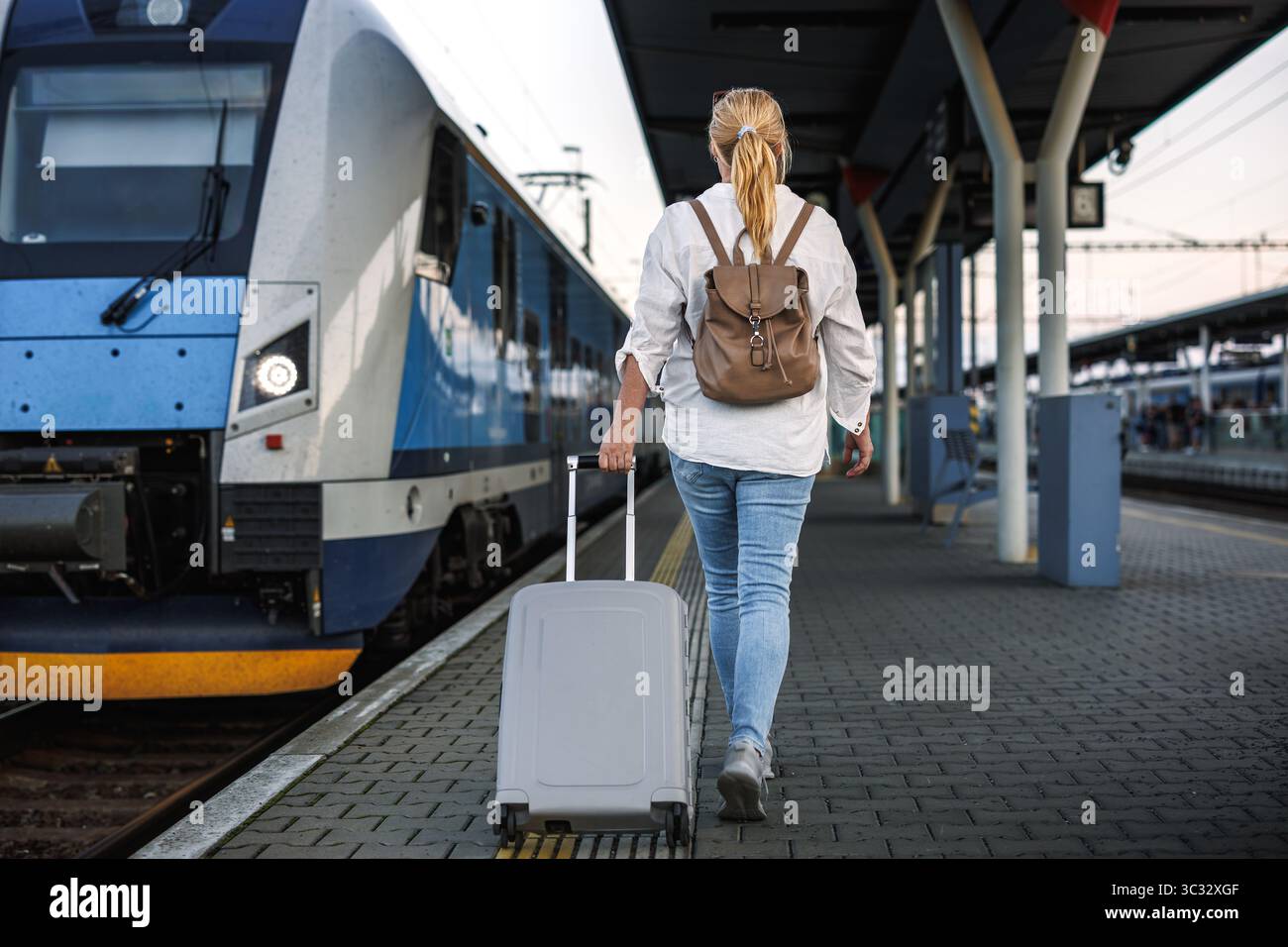 Reisen Sie mit dem Zug. Frau mit Koffer, die am Bahnsteig im Zug einsteigen will. Alleinreisende Stockfoto