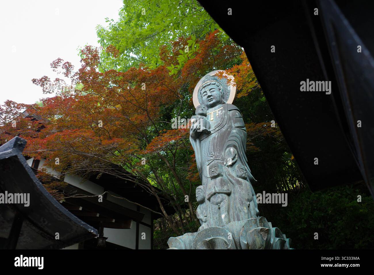 Eine friedliche Bronzestatue von Kannon, der buddhistischen Göttin der Gnade, die ein Kind im Myoen-JI-Tempel in Japan hält. Umgeben von bunten Bäumen Stockfoto
